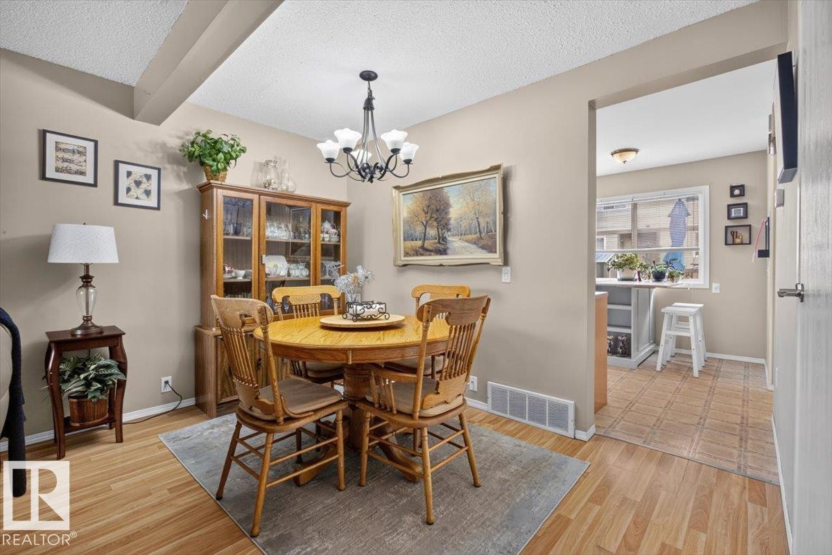 Dining area featuring wood-finish flooring, a contemporary chandelier, and a built-in display cabinet - 27 Walden Park, St. Albert, AB