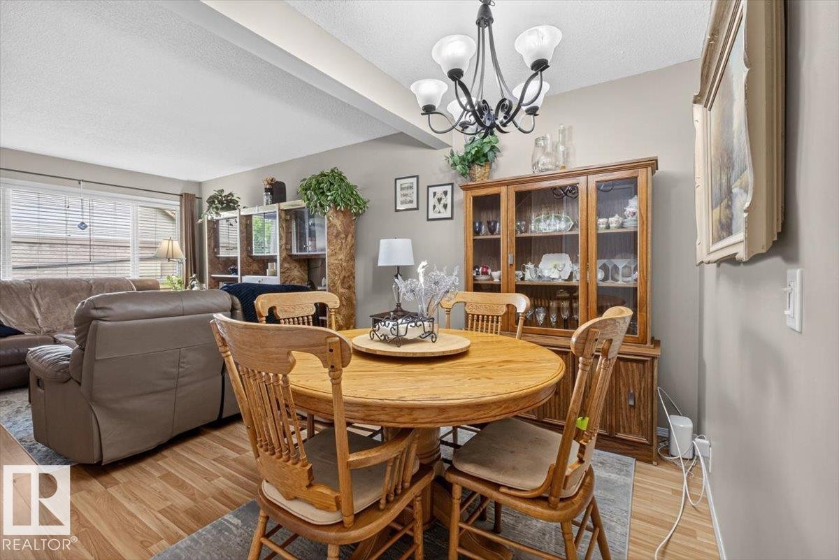 Open-concept living and dining area featuring wood-finish flooring, a decorative chandelier, and a large window with horizontal blinds - 27 Walden Park, St. Albert, AB