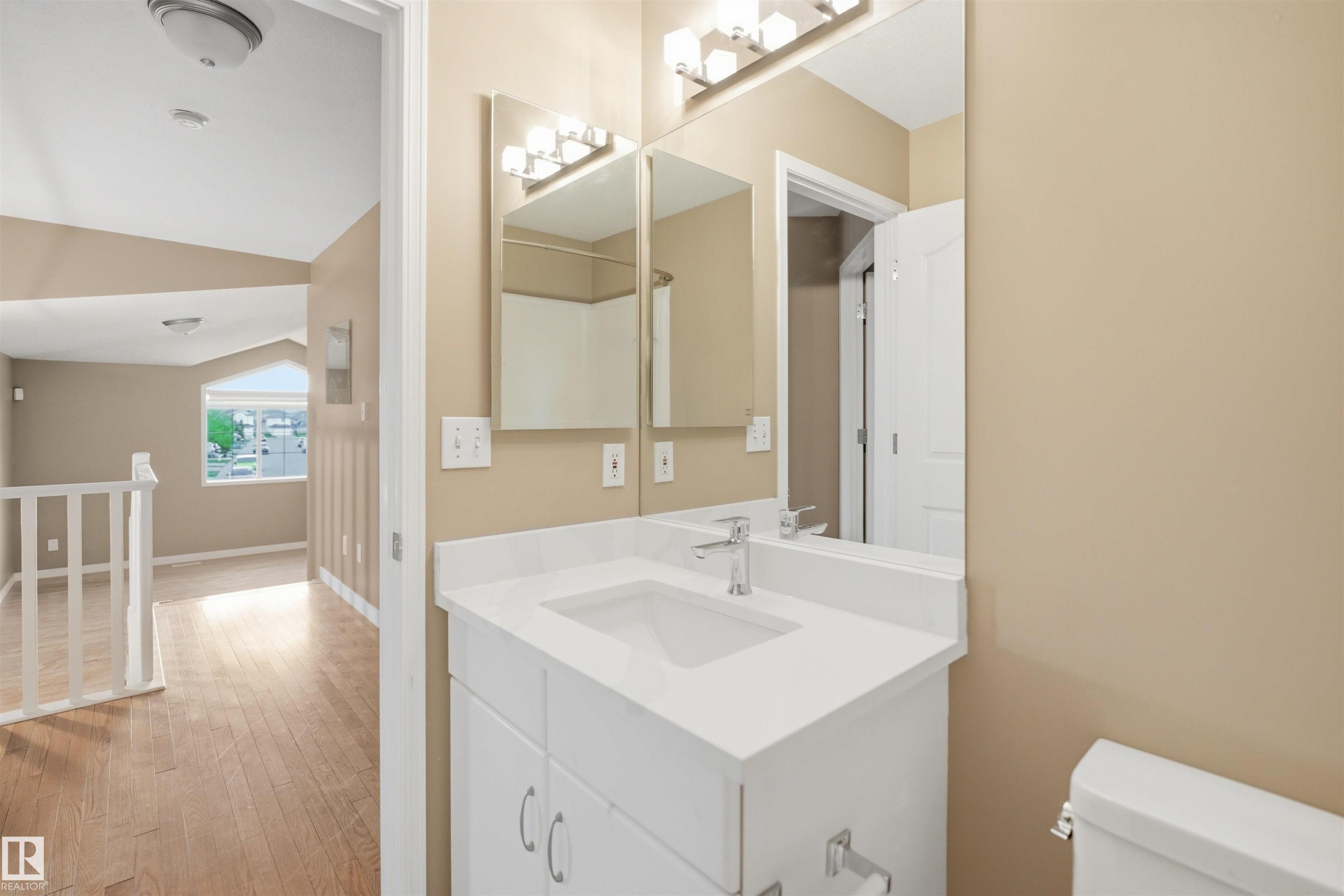 Bathroom featuring a single vanity with a white countertop and integrated sink, a large wall mirror, and a modern light fixture - 2610 33A Street, Edmonton, AB - Indoor Photo Showing Bathroom