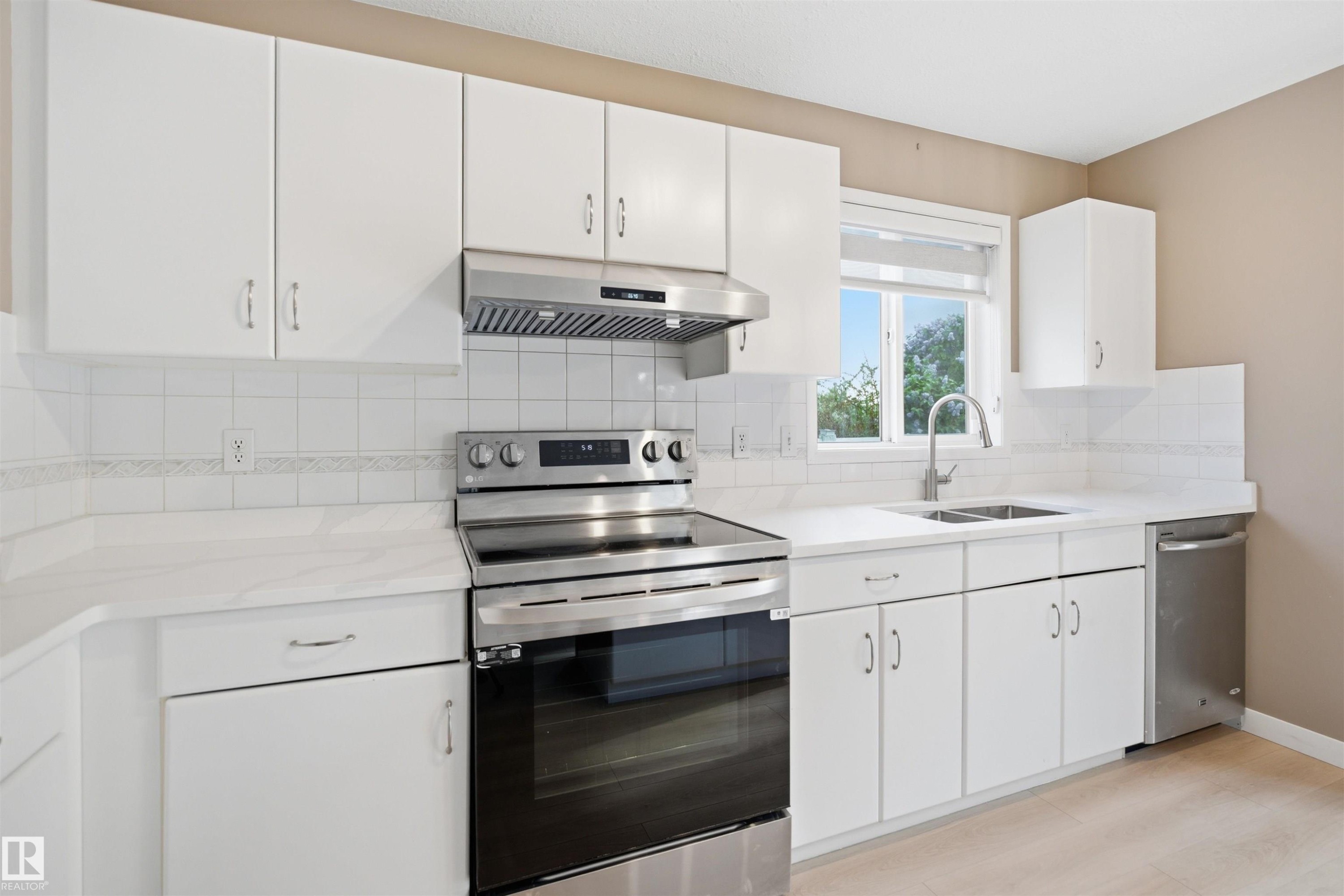 Contemporary kitchen featuring white cabinetry, stainless steel appliances, a tile backsplash, and light-toned countertops - 2610 33A Street, Edmonton, AB - Indoor Photo Showing Kitchen With Double Sink