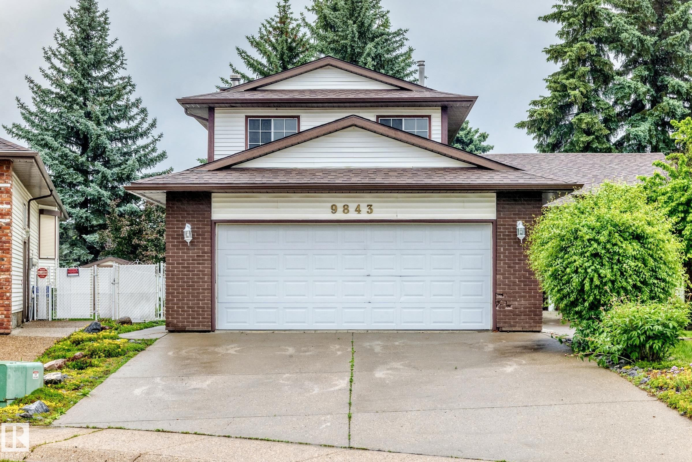 Two-story residence featuring a two-car garage with white door, brick accents, and neutral siding - 9843 188 Street, Edmonton, AB