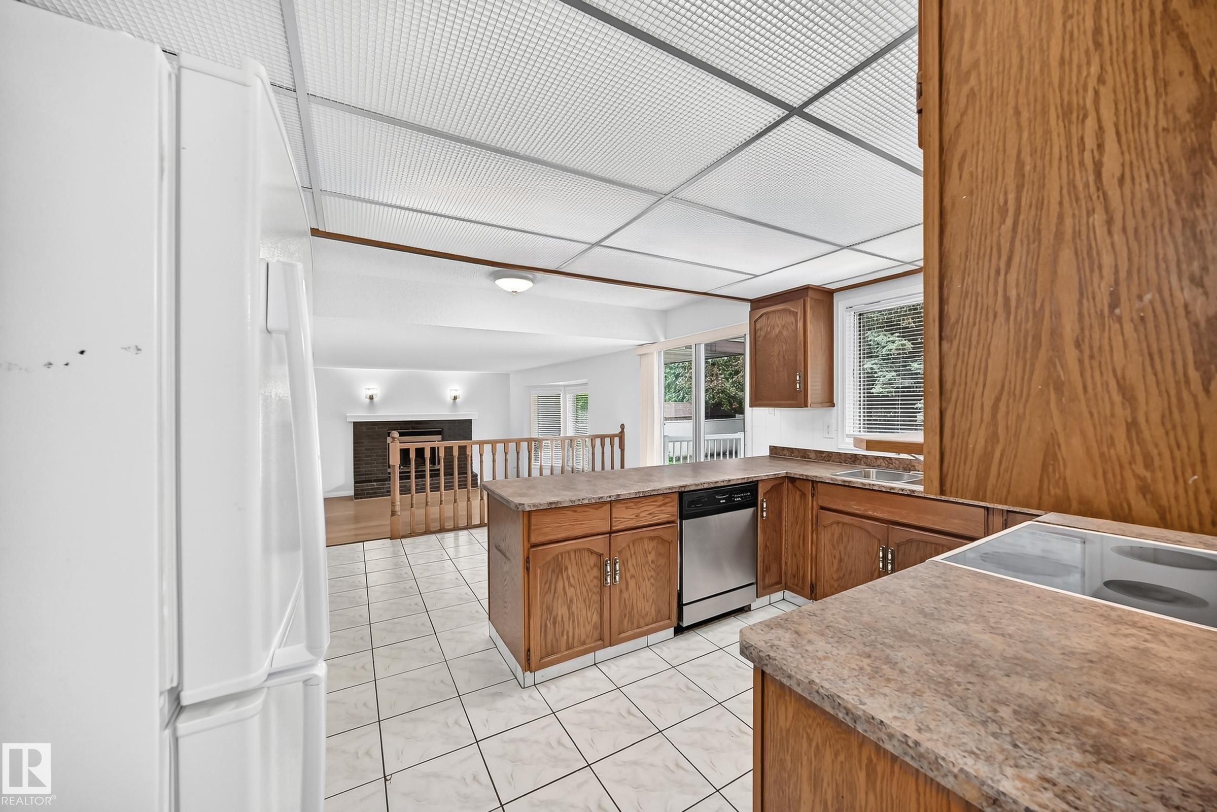 Kitchen featuring wood cabinetry, stone-look countertops, and white tile flooring - 9843 188 Street, Edmonton, AB