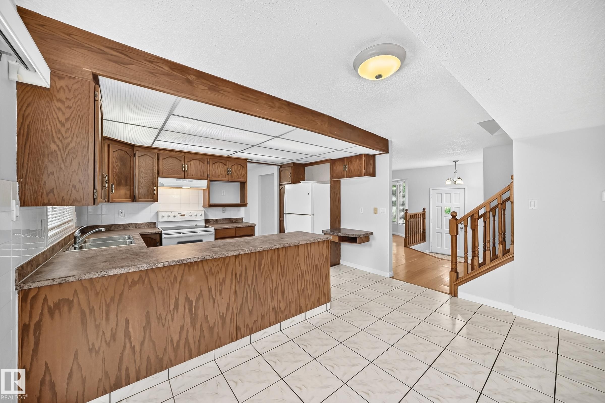 Kitchen featuring wood-finish cabinetry, a white tile backsplash, and a built-in double sink - 9843 188 Street, Edmonton, AB