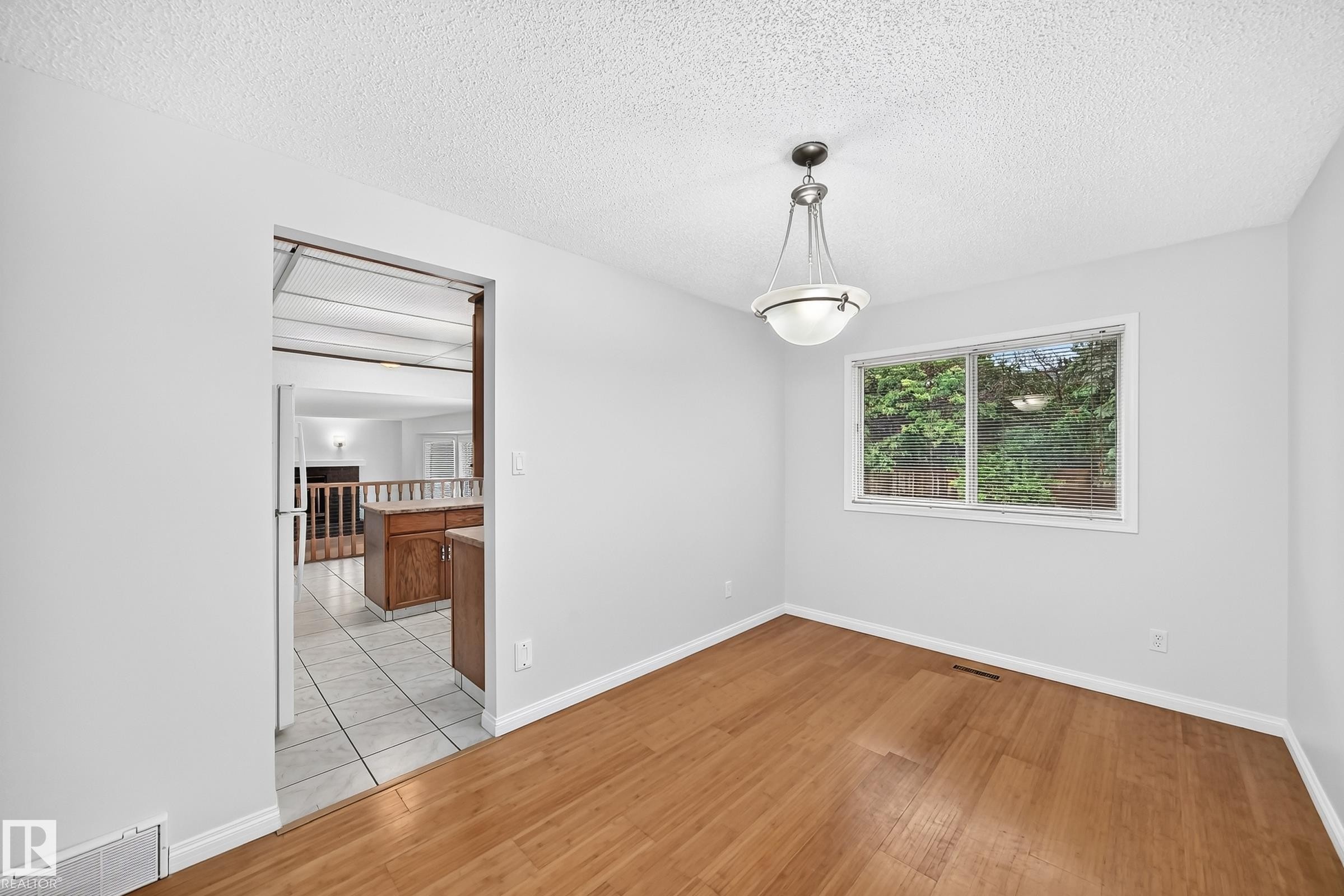 Dining area featuring wood-finish flooring, a contemporary pendant light fixture, and a window with exterior tree views - 9843 188 Street, Edmonton, AB
