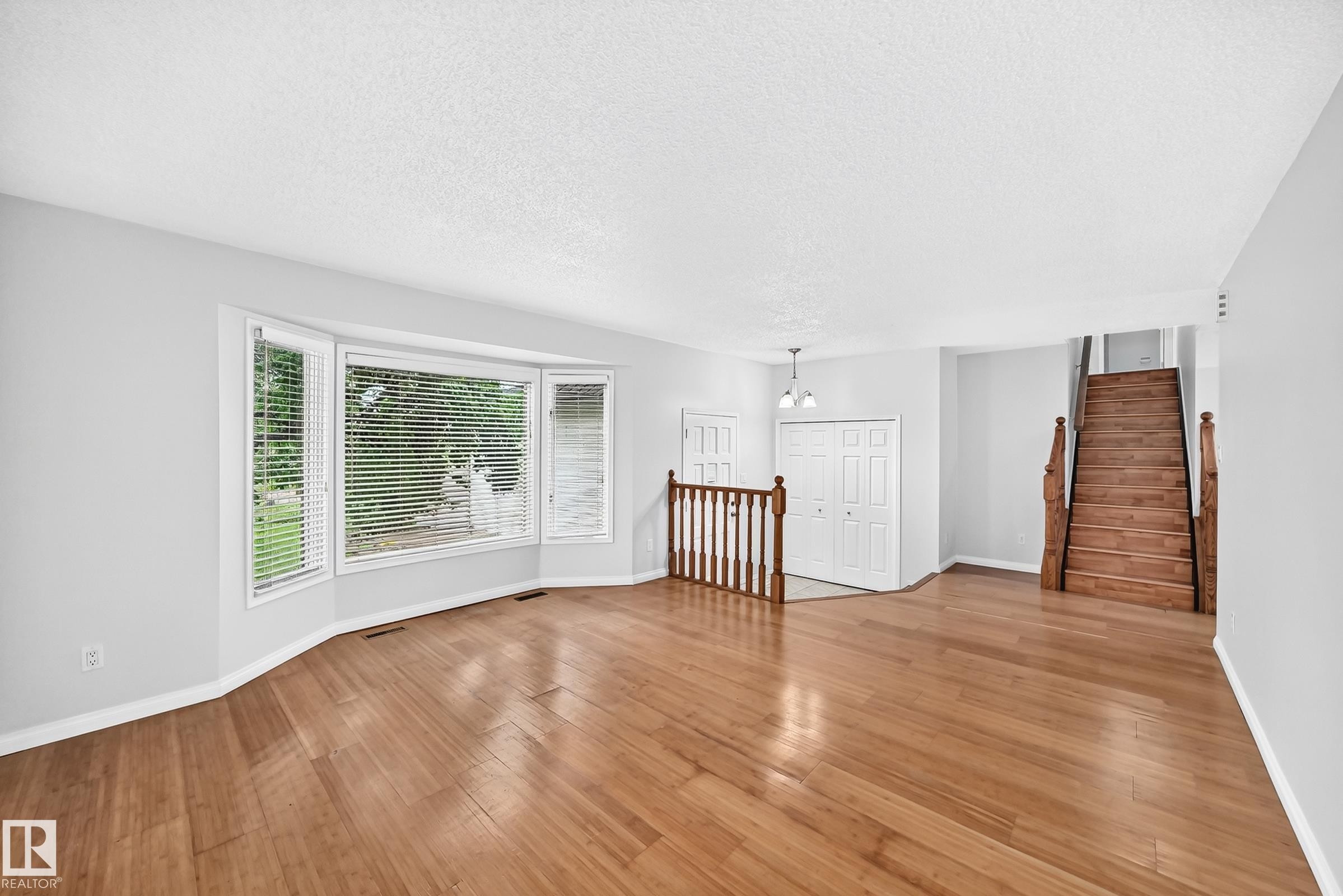 Spacious living area featuring wood-finish flooring, a prominent bay window with blinds, and white trim - 9843 188 Street, Edmonton, AB