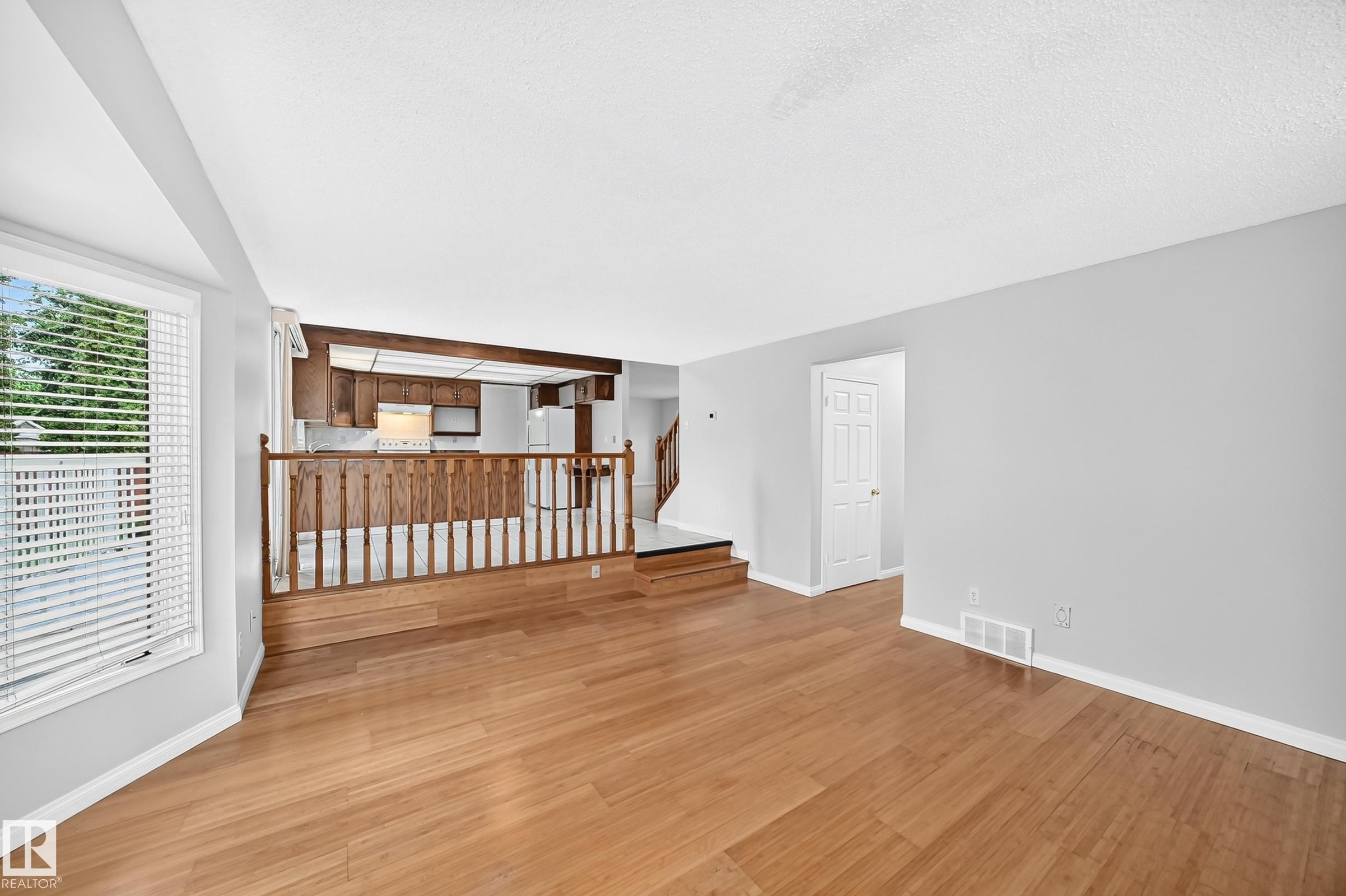 Living area with wood-finish flooring, light grey walls, and a large window with blinds - 9843 188 Street, Edmonton, AB