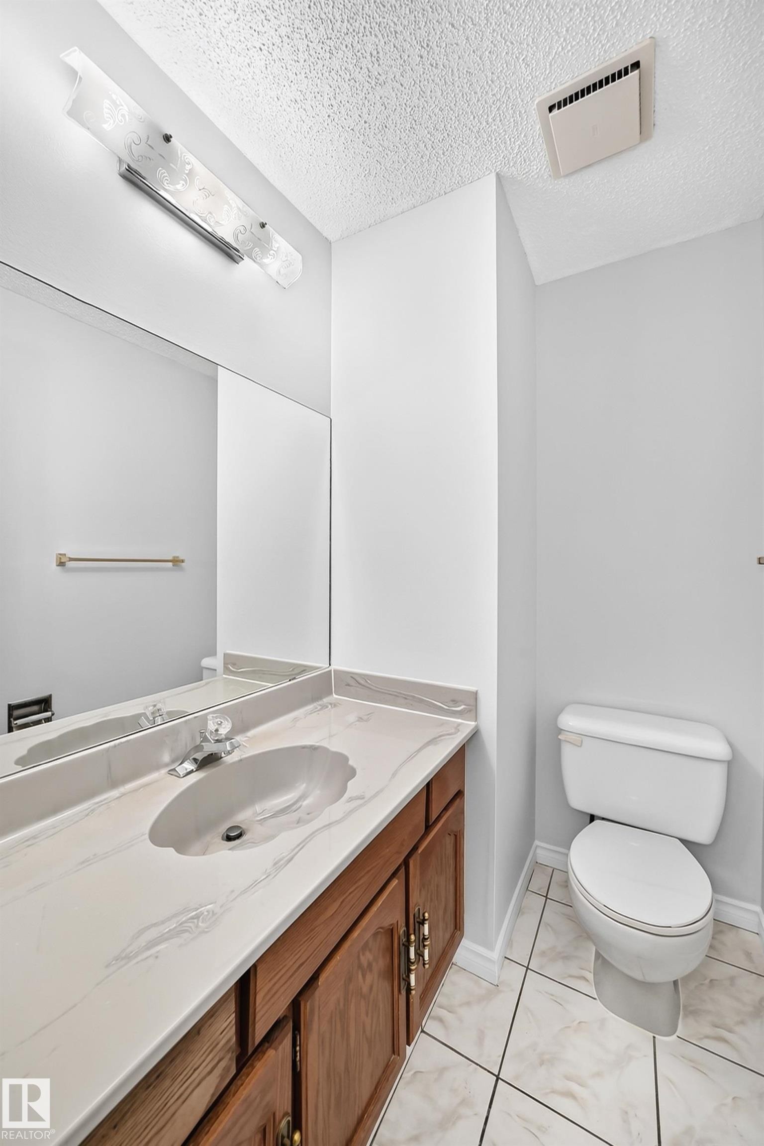 Bathroom vanity with wood-finish cabinetry, a patterned countertop, an integrated sink, and a wall-mounted light fixture - 9843 188 Street, Edmonton, AB