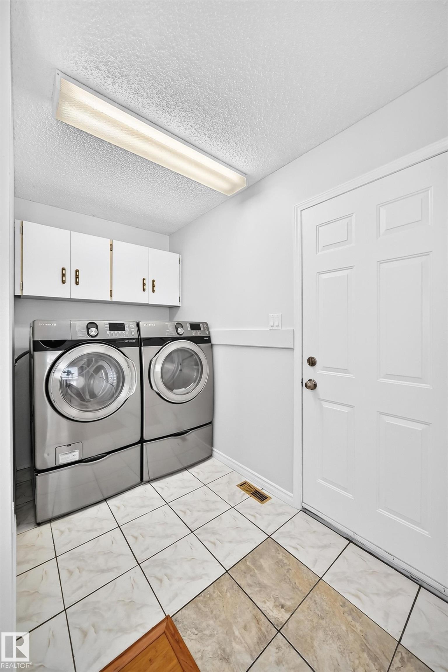 Laundry area with white cabinetry, a white paneled door, and two-tone tile flooring - 9843 188 Street, Edmonton, AB