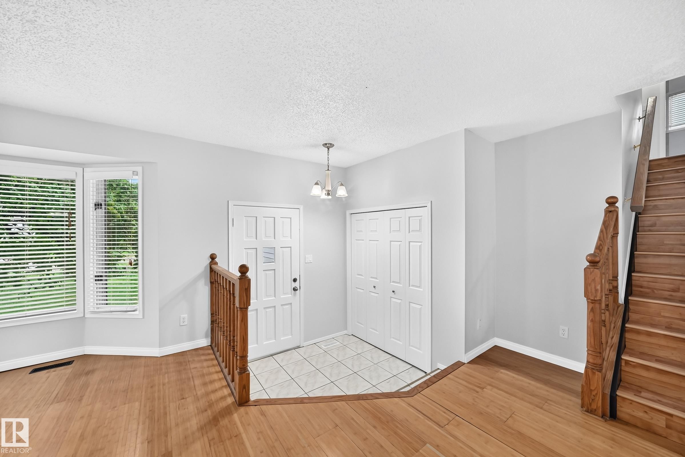 Entryway featuring wood-finish flooring, a bay window with blinds, and a tiled landing - 9843 188 Street, Edmonton, AB