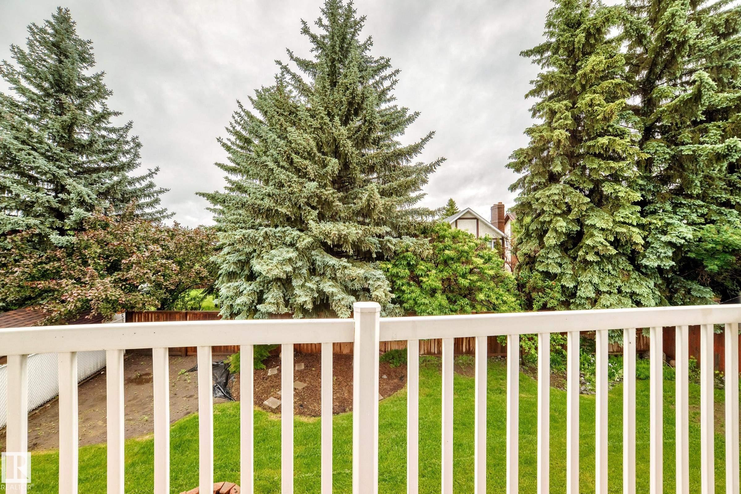 White picket railing overlooking a verdant backyard with mature evergreen trees and a wood fence - 9843 188 Street, Edmonton, AB