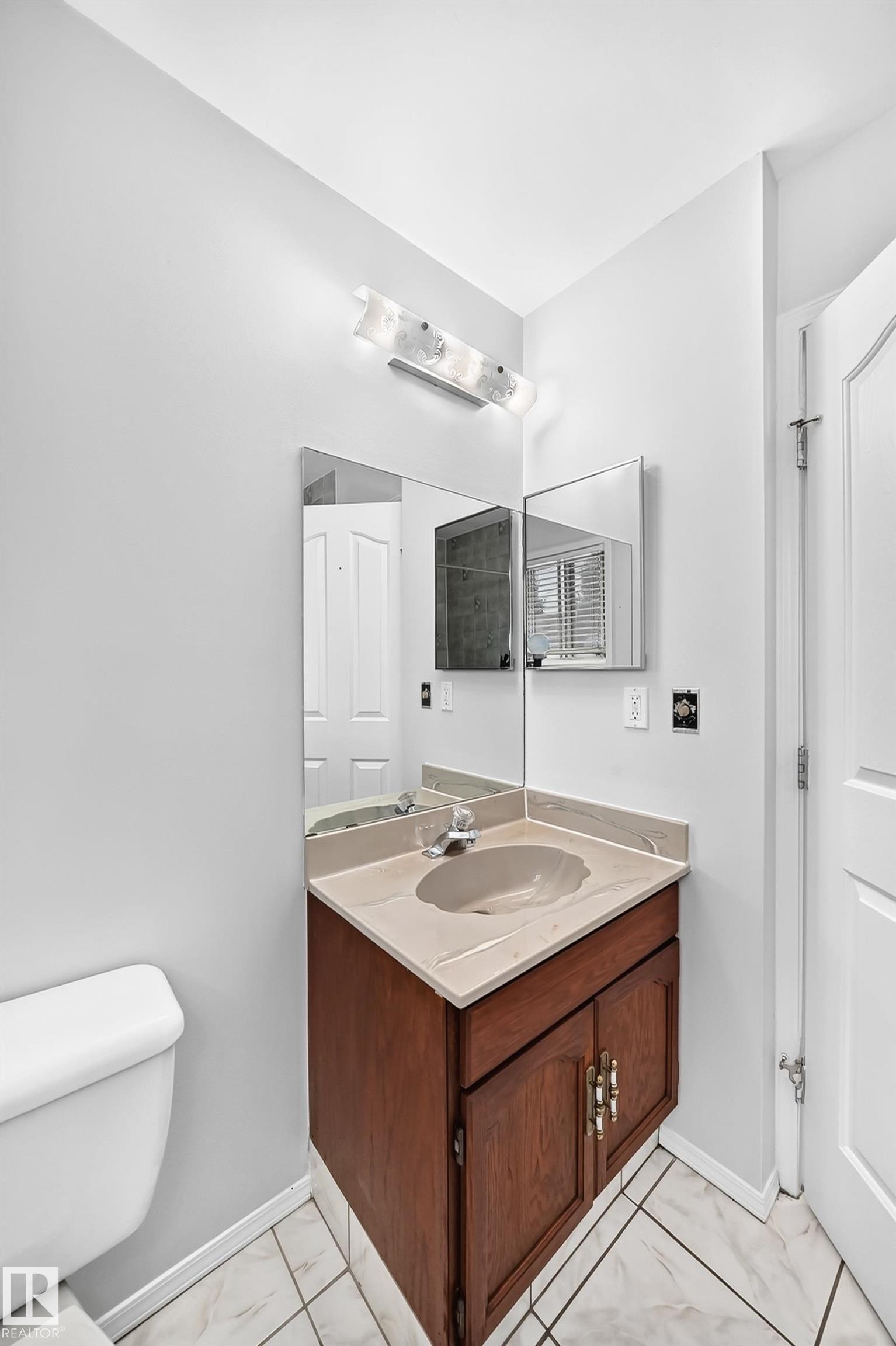 Vanity with a wood-finish cabinet and integrated sink, complemented by a polished chrome faucet - 9843 188 Street, Edmonton, AB