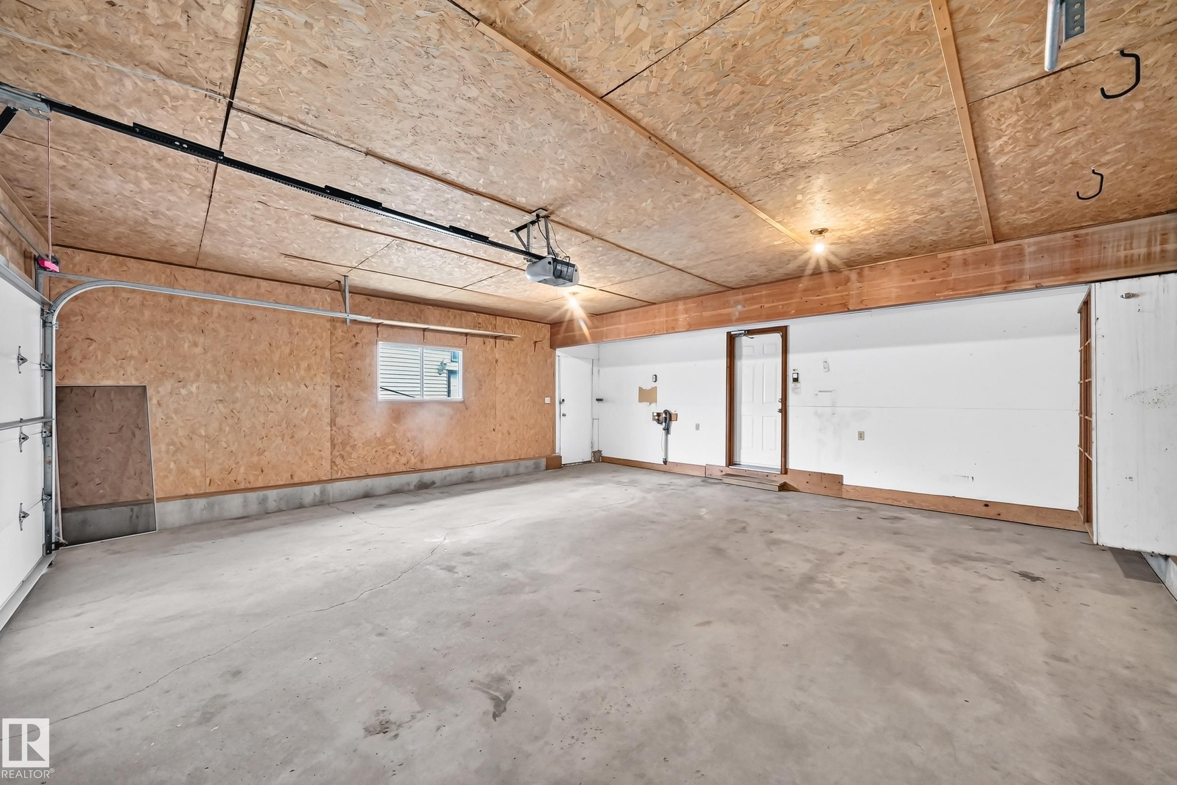 Spacious garage featuring a concrete floor, exposed wood ceiling, and built-in shelving - 9843 188 Street, Edmonton, AB