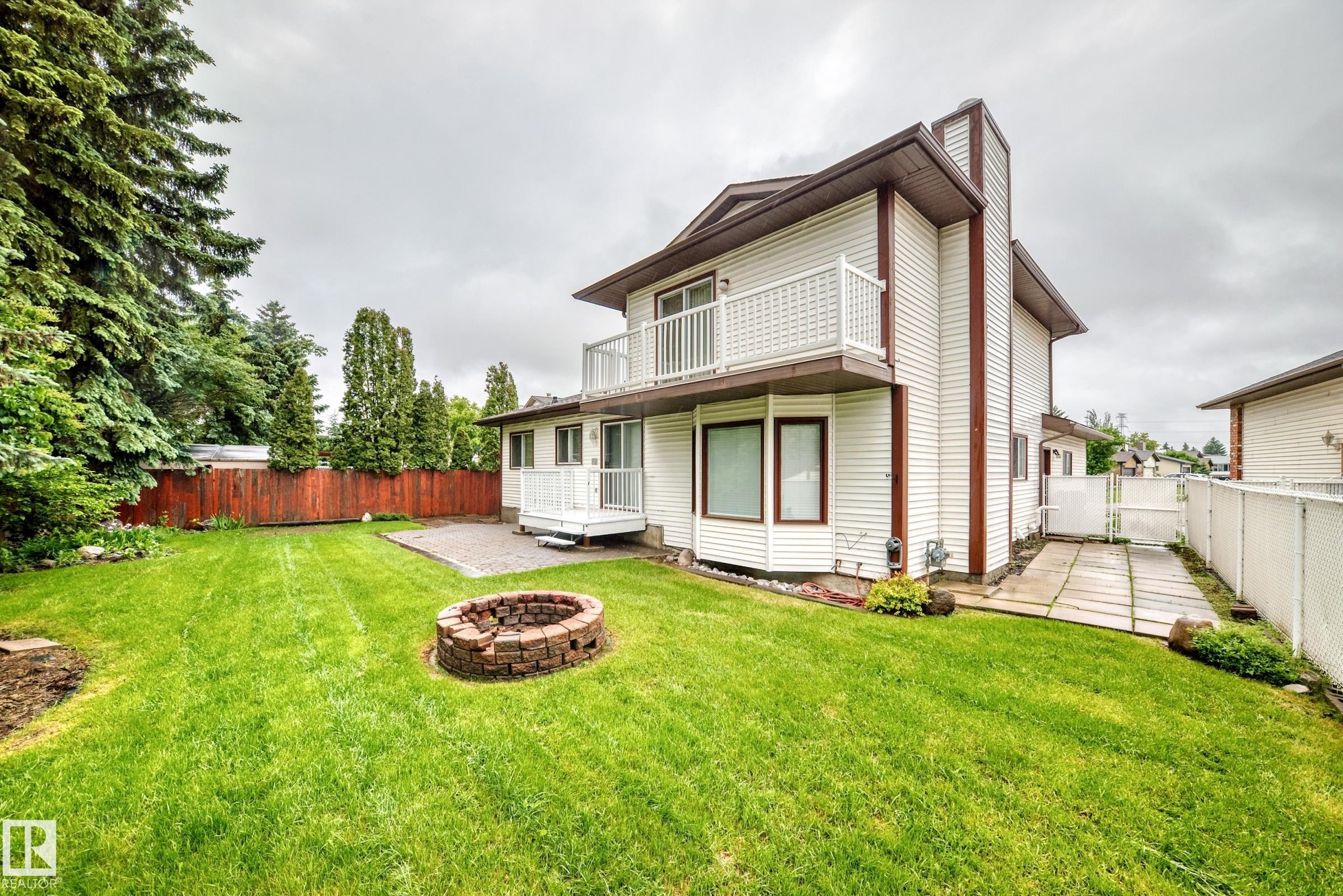 Expansive backyard featuring a brick fire pit, a paved patio area, and a white vinyl-sided exterior - 9843 188 Street, Edmonton, AB