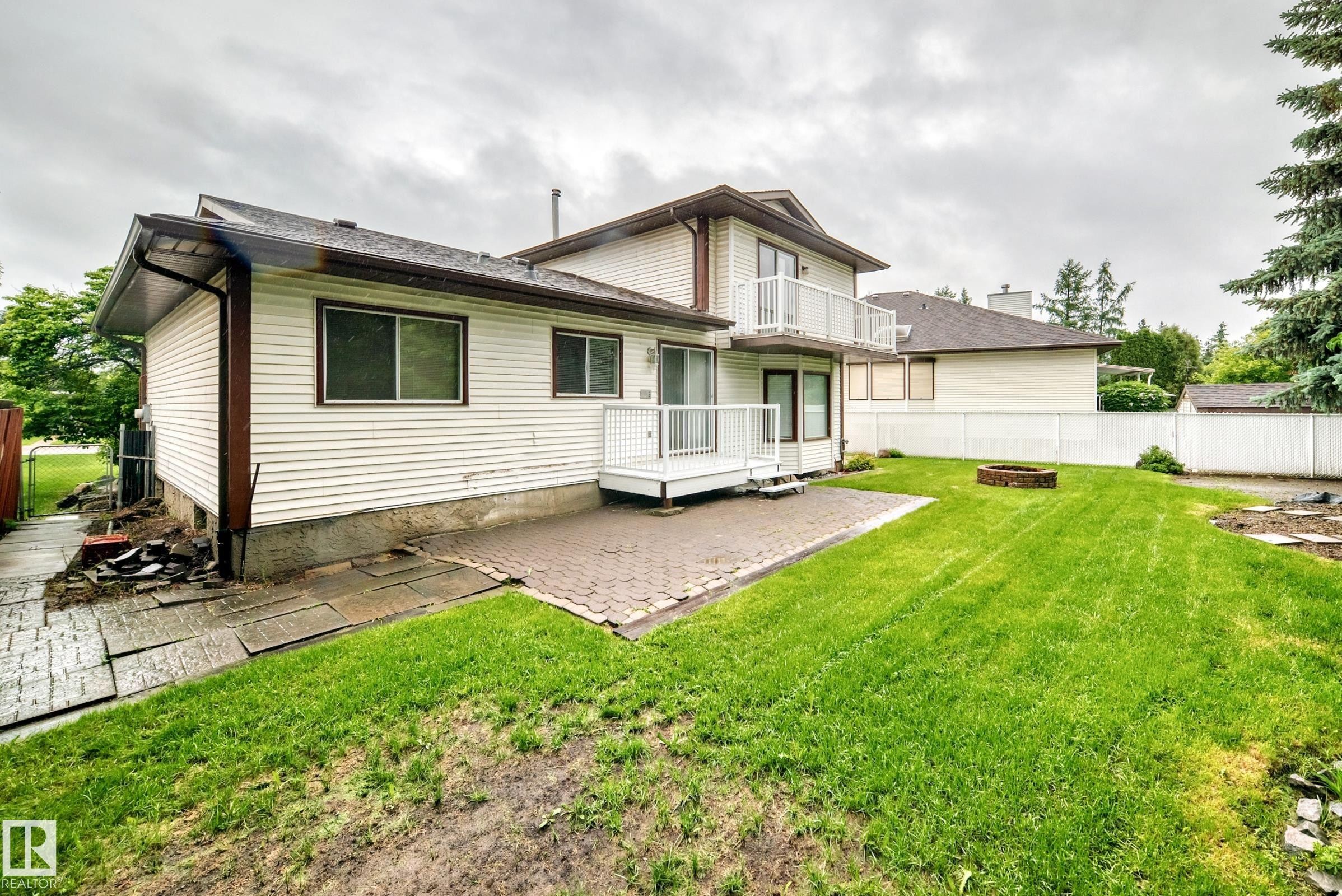 Expansive backyard featuring a lush lawn, paver patio, second-story balcony with white railing, and a ground-level deck with white railing - 9843 188 Street, Edmonton, AB
