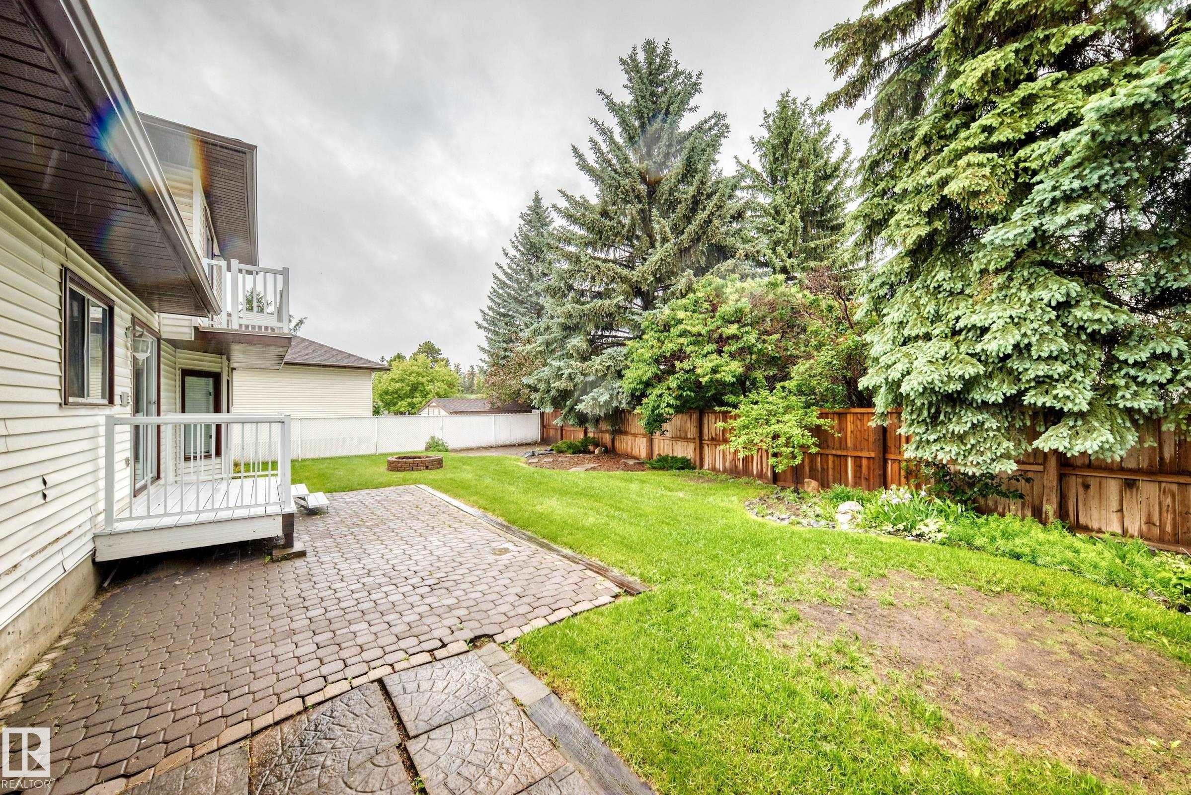 Expansive backyard featuring a stone paver patio, a raised deck, and a fire pit - 9843 188 Street, Edmonton, AB
