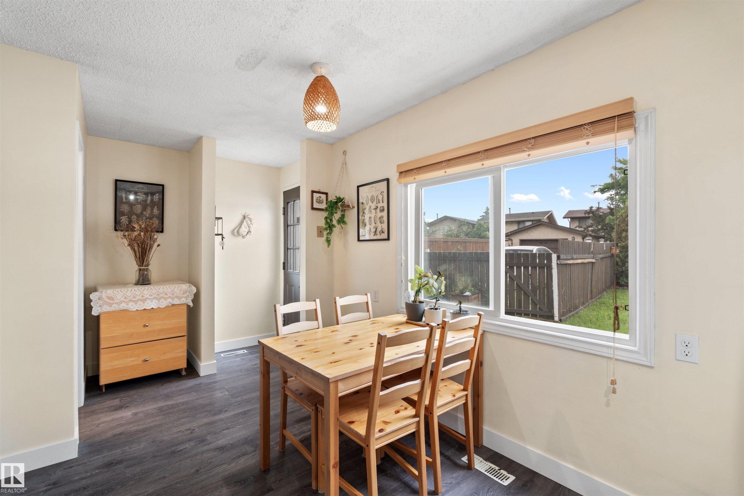 Dining area featuring wood-finish flooring, a large window with wooden blinds, and a woven pendant light fixture - 359 Kirkpatrick Crescent, Edmonton, AB