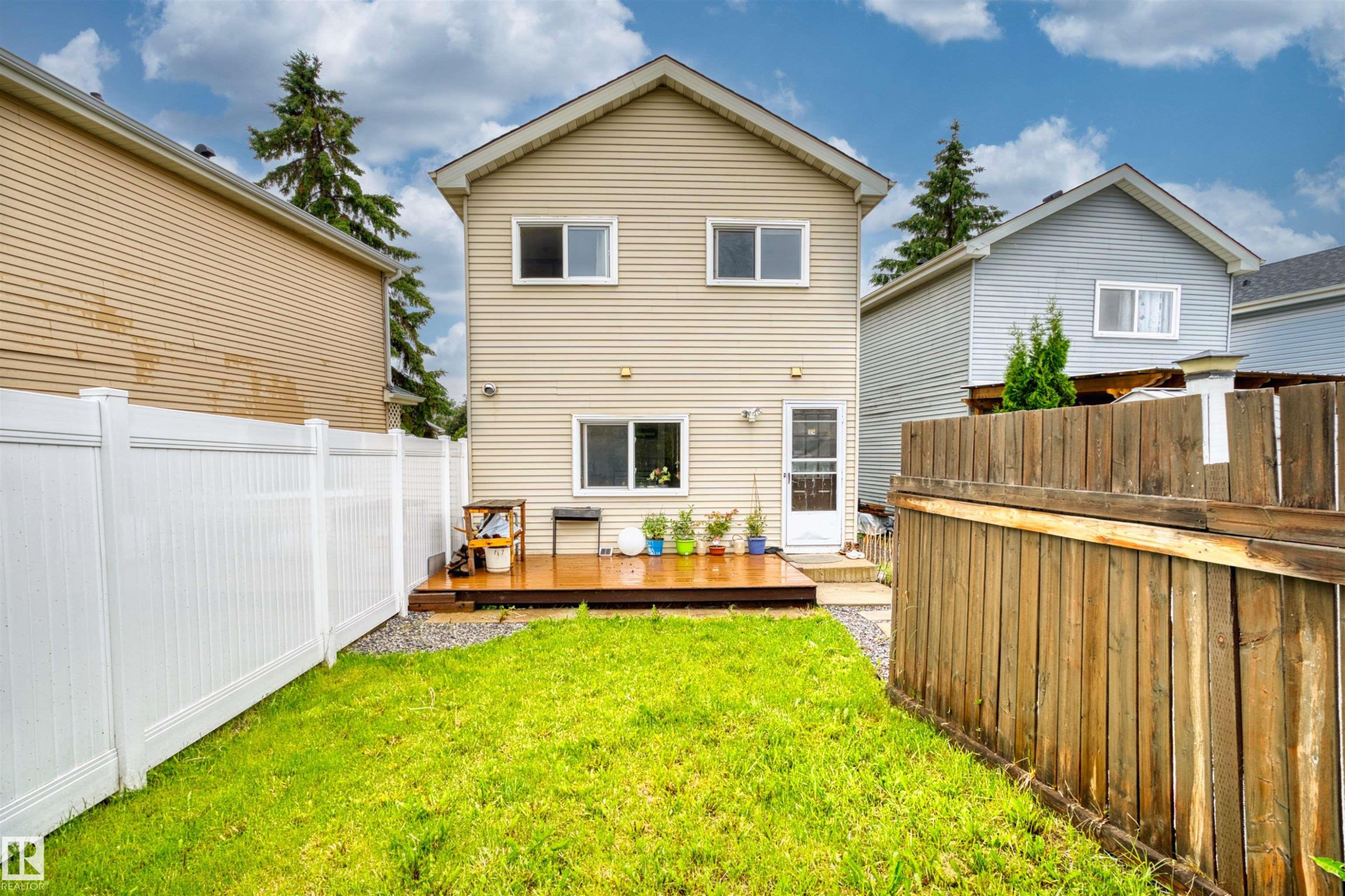 Expansive backyard featuring a manicured lawn, a wooden deck, a white vinyl fence, and a wooden privacy fence - 359 Kirkpatrick Crescent, Edmonton, AB