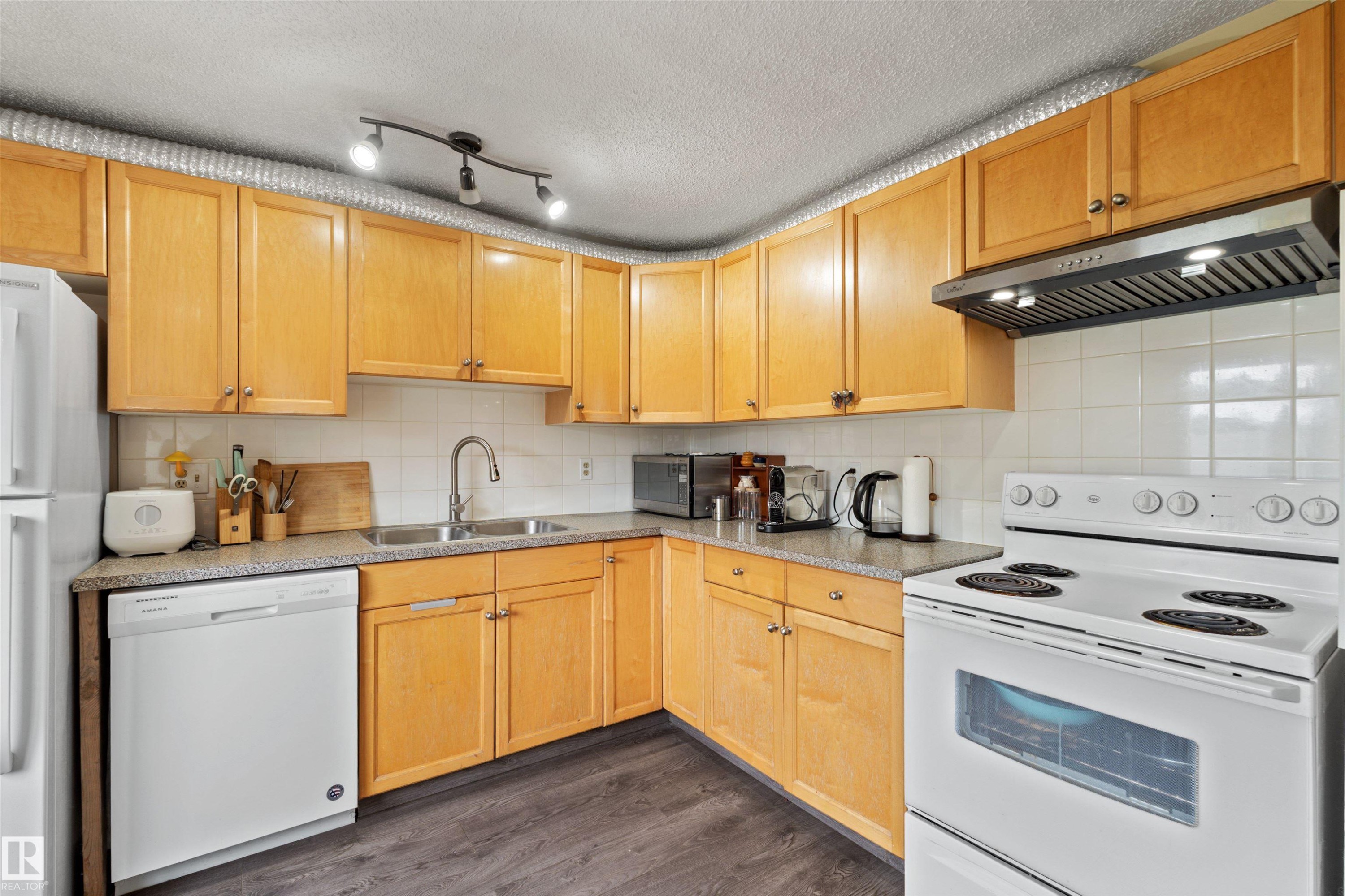 Kitchen featuring wood-finish cabinetry, white tile backsplash, a stainless steel sink with a gooseneck faucet, a built-in dishwasher, and wood-finish flooring - 359 Kirkpatrick Crescent, Edmonton, AB