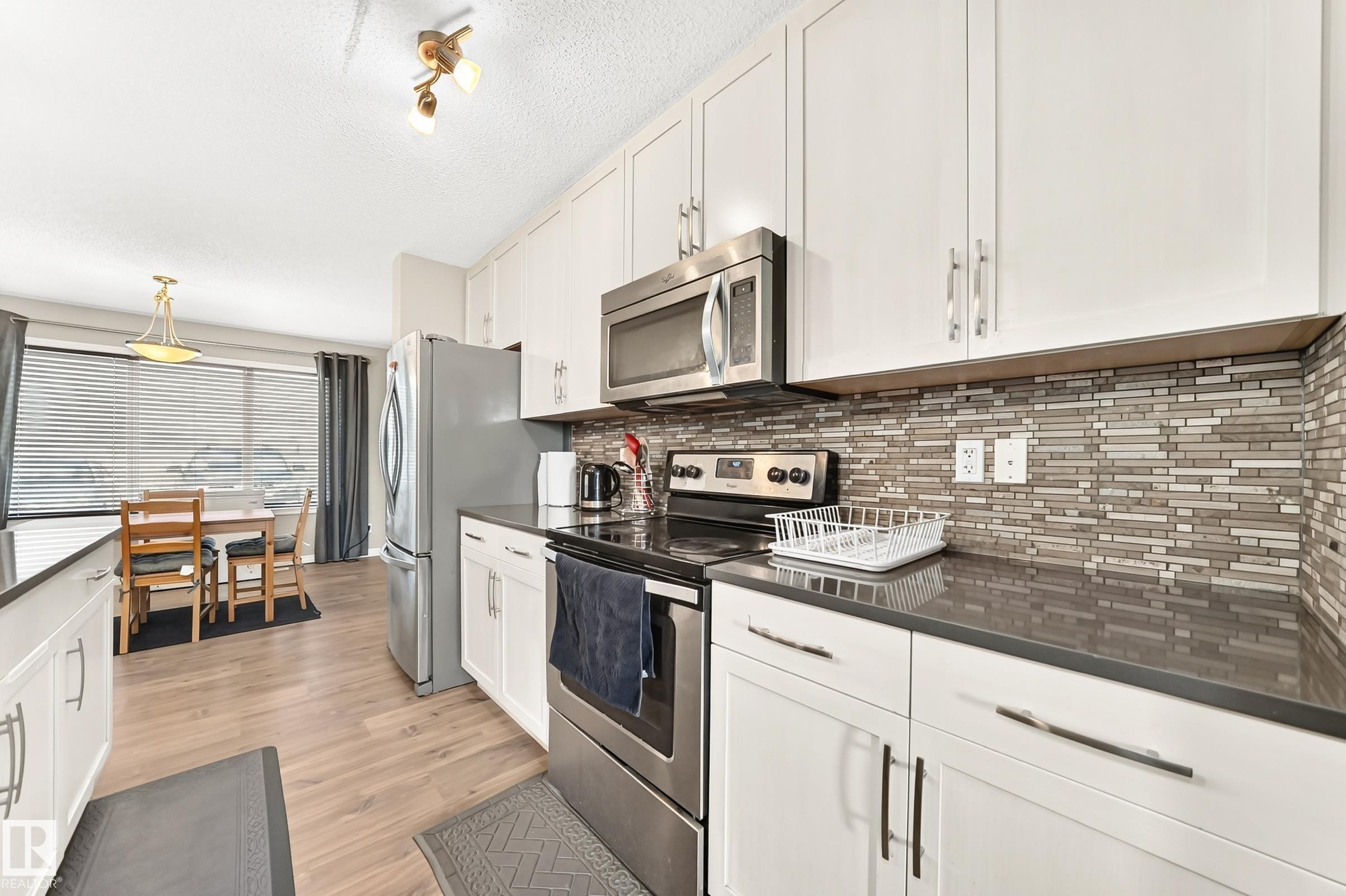 Kitchen featuring white cabinetry, stainless steel appliances, dark countertops, and a mosaic tile backsplash - 875 Chappelle Link Link Sw, Edmonton, AB