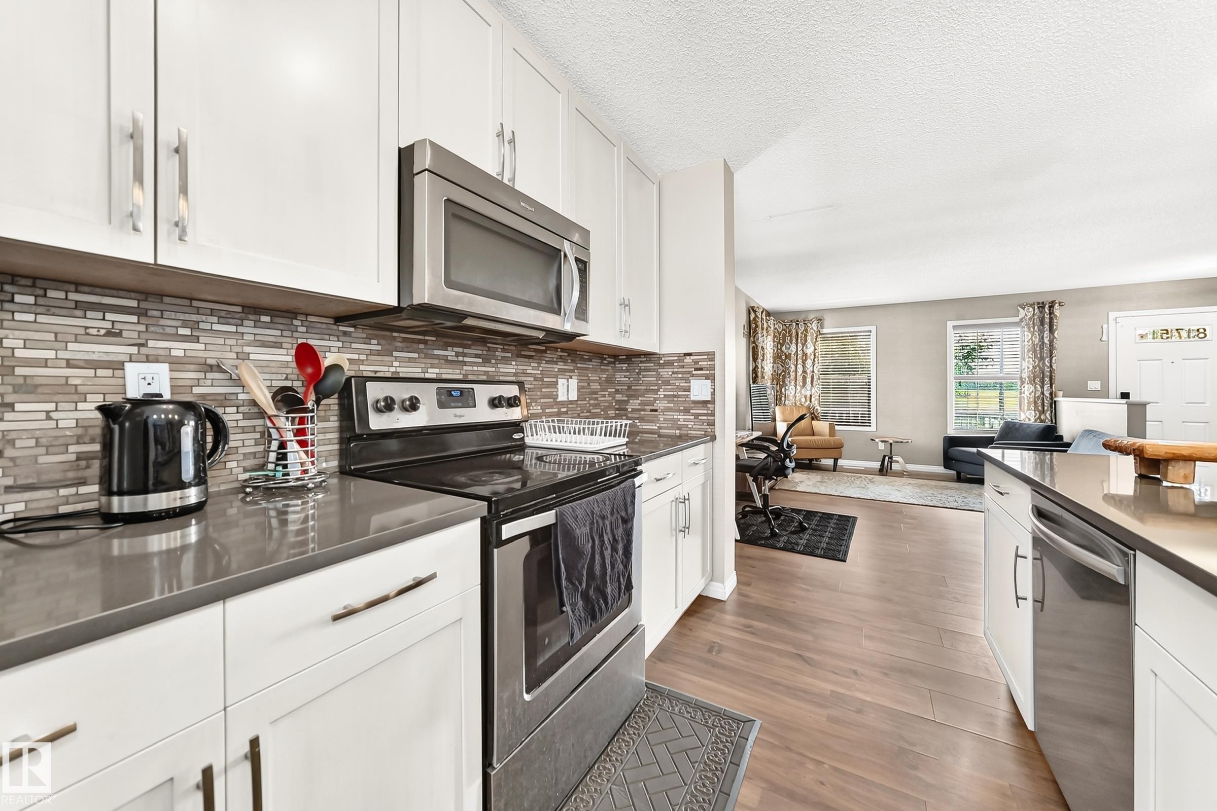 Contemporary kitchen with white cabinetry, stainless steel appliances, dark countertops, and a mosaic tile backsplash - 875 Chappelle Link Link Sw, Edmonton, AB