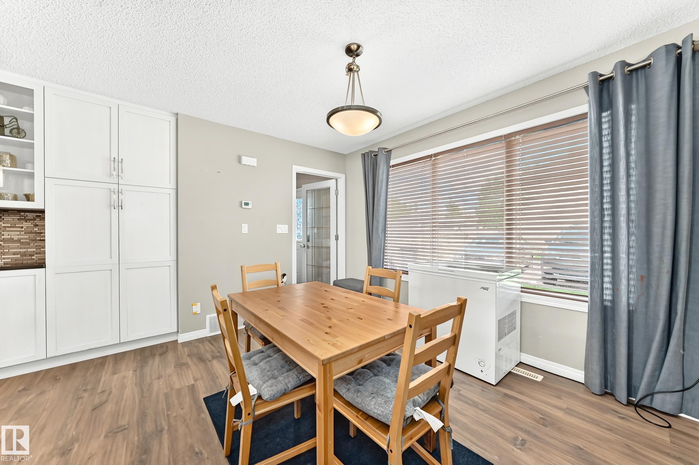 Dining area featuring wood-finish flooring, a contemporary ceiling light fixture, and white built-in cabinetry with both solid and glass-front doors - 875 Chappelle Link Link Sw, Edmonton, AB