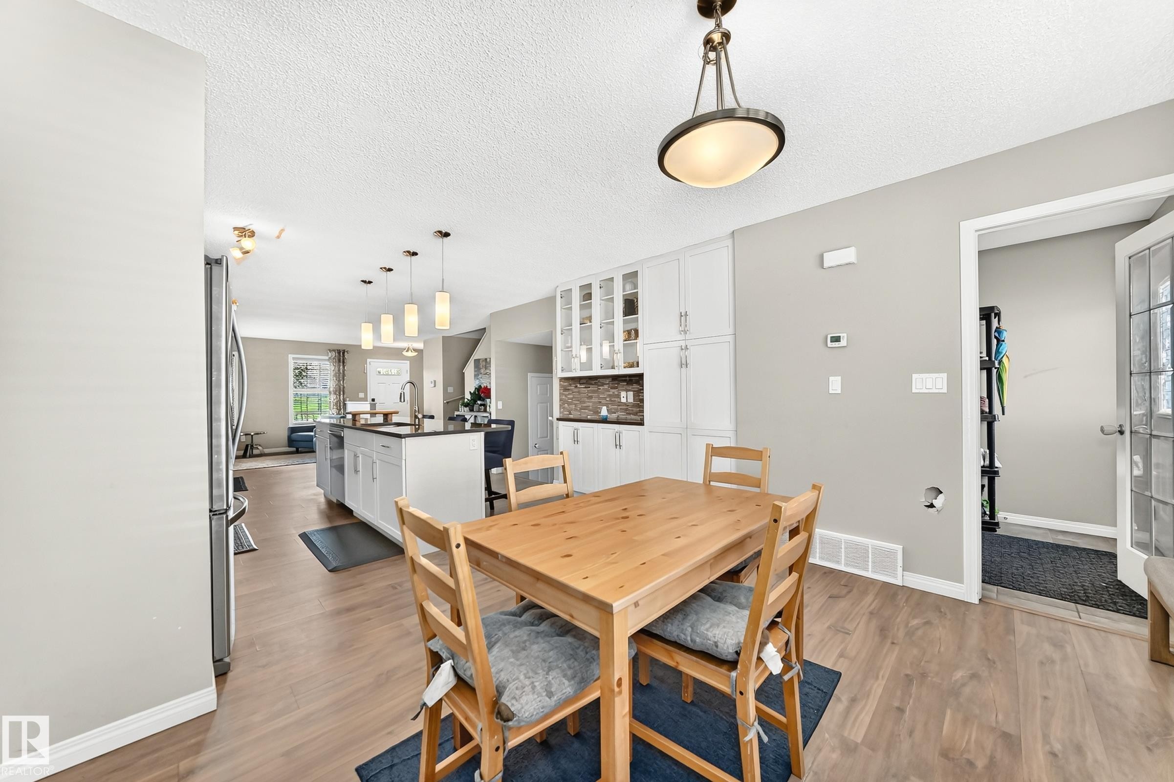 Open-concept kitchen and dining area featuring wood-finish flooring, white cabinetry, a kitchen island with pendant lighting, and a dark countertop - 875 Chappelle Link Link Sw, Edmonton, AB