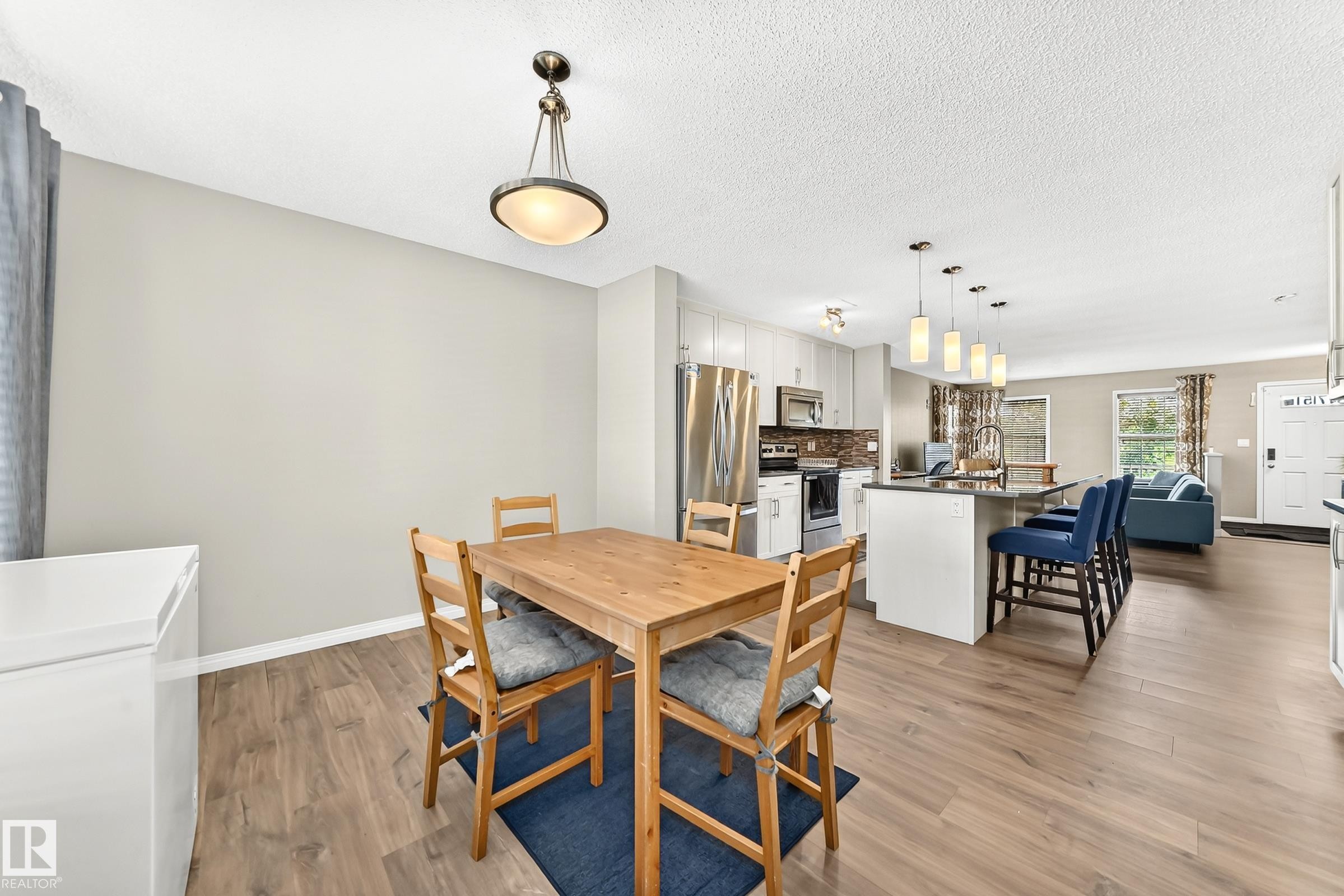 Open-concept interior featuring wood-finish flooring, a kitchen island with pendant lighting, stainless steel appliances, and light-toned cabinetry - 875 Chappelle Link Link Sw, Edmonton, AB