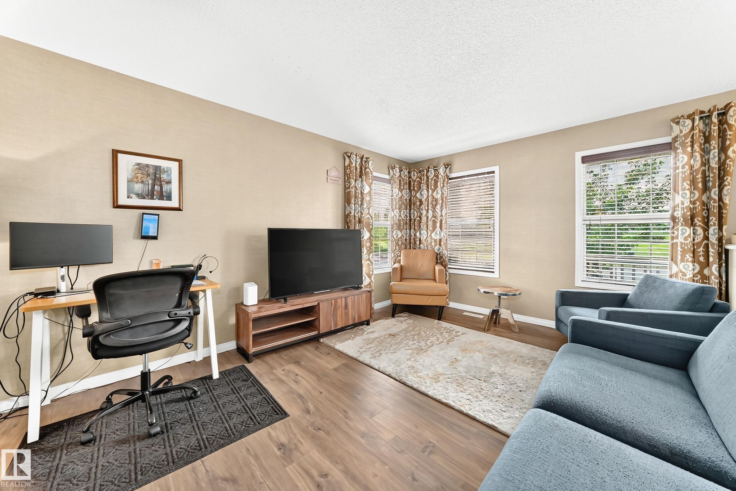 Spacious living area featuring wood-finish flooring, neutral wall tones, and multiple windows with blinds - 875 Chappelle Link Link Sw, Edmonton, AB