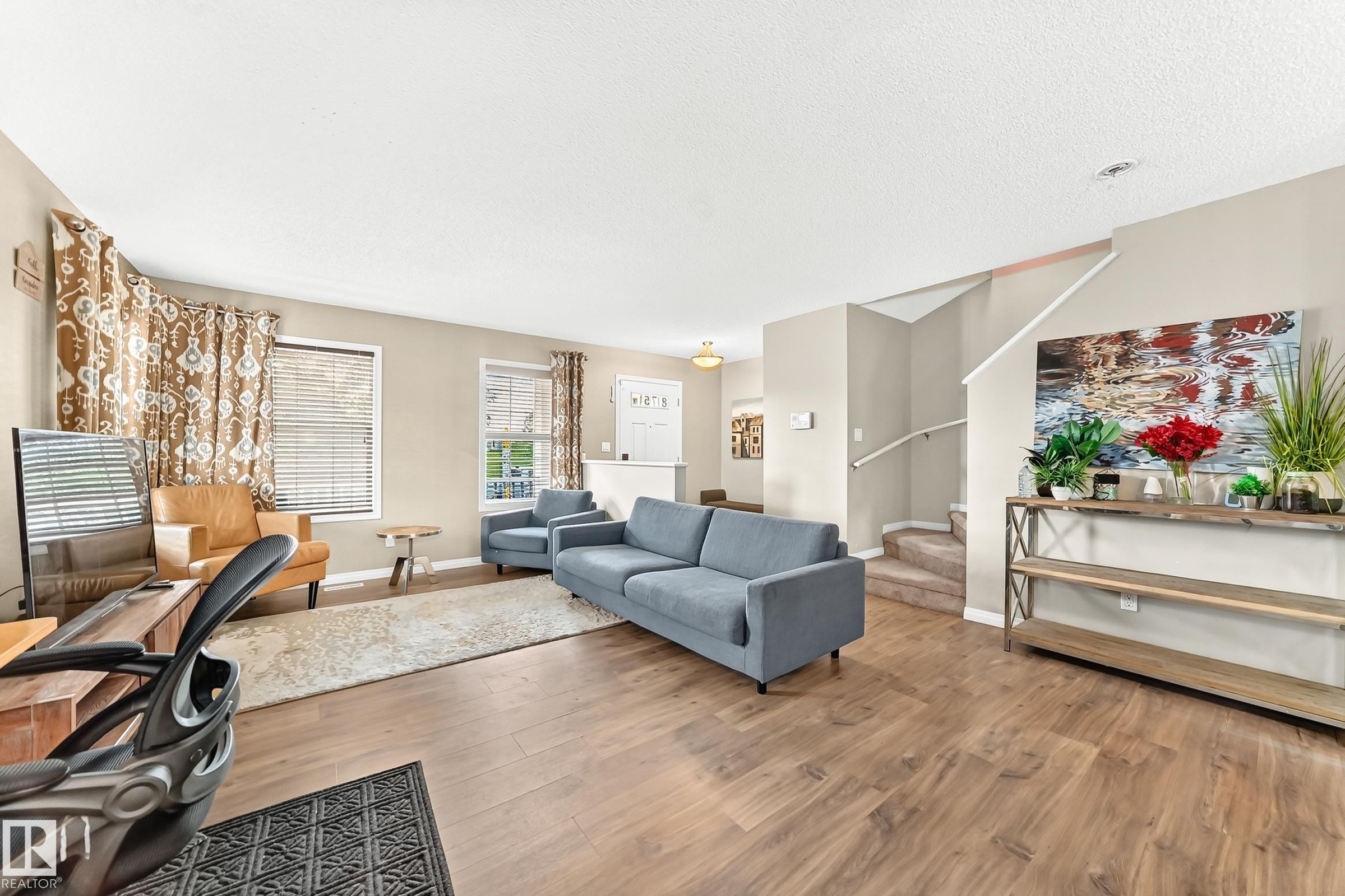Spacious living area featuring wood-finish flooring, neutral wall tones, and multiple windows - 875 Chappelle Link Link Sw, Edmonton, AB
