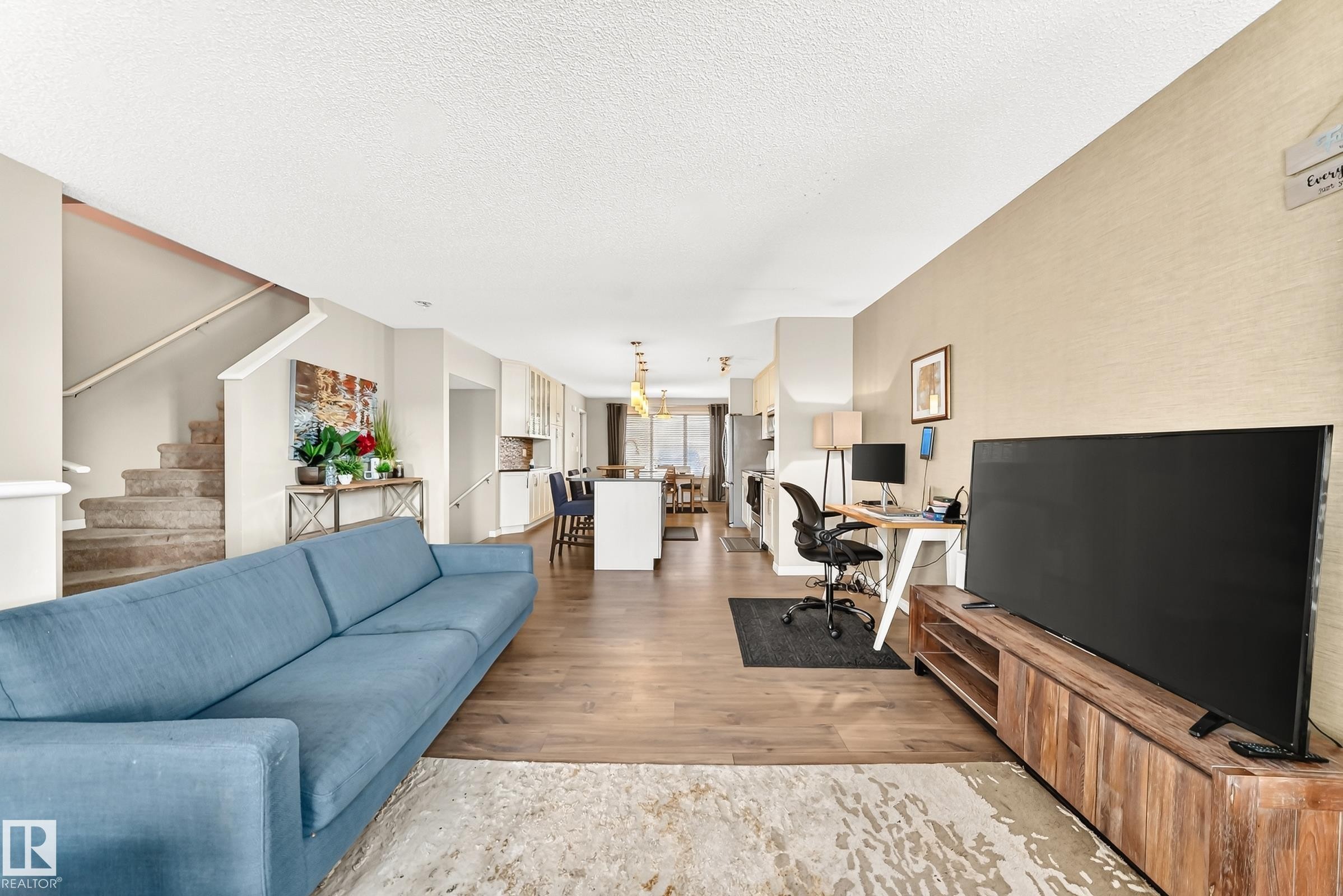 Open-concept living space featuring wood-finish flooring, a neutral color palette, a staircase with carpeted treads, and recessed lighting - 875 Chappelle Link Link Sw, Edmonton, AB