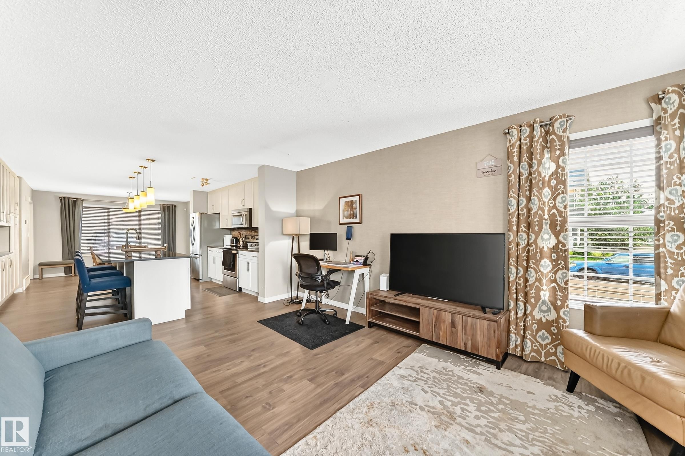 Open-concept living area with wood-finish flooring, a kitchen island, and a dedicated workspace - 875 Chappelle Link Link Sw, Edmonton, AB