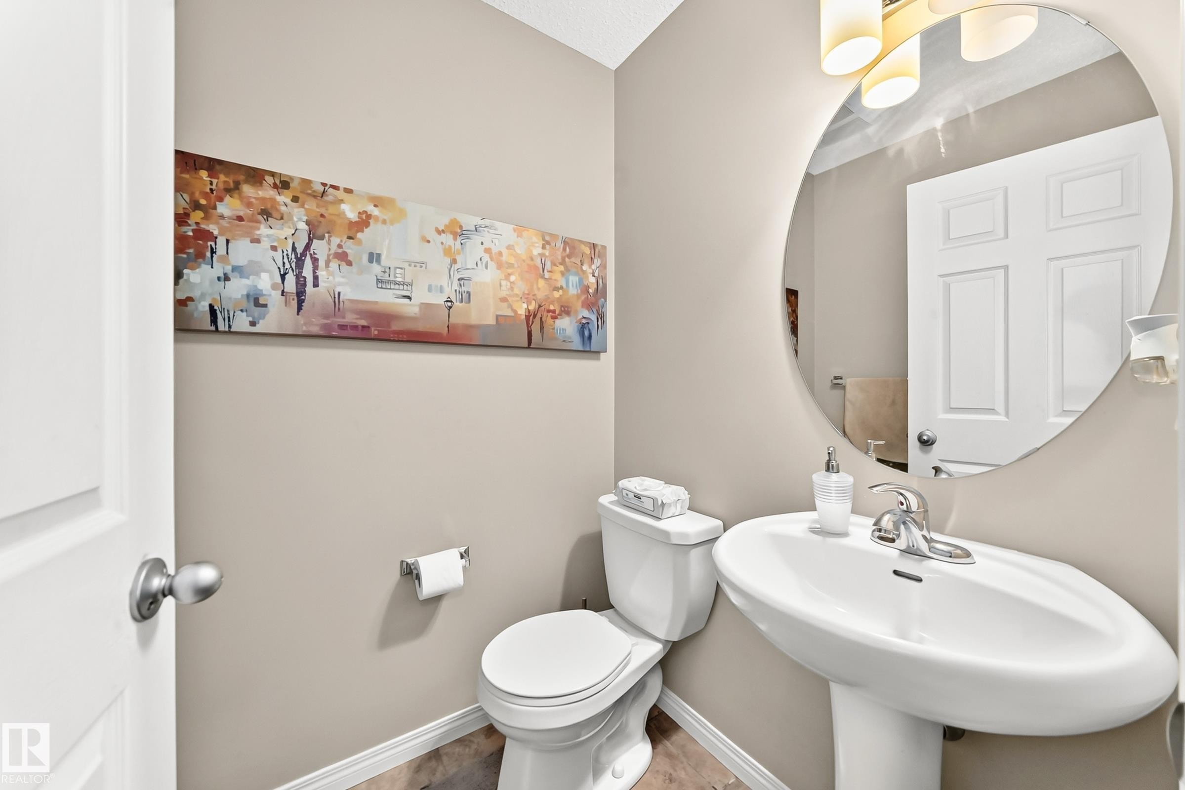 Pedestal sink with chrome faucet, circular mirror, and wall-mounted light fixture - 875 Chappelle Link Link Sw, Edmonton, AB