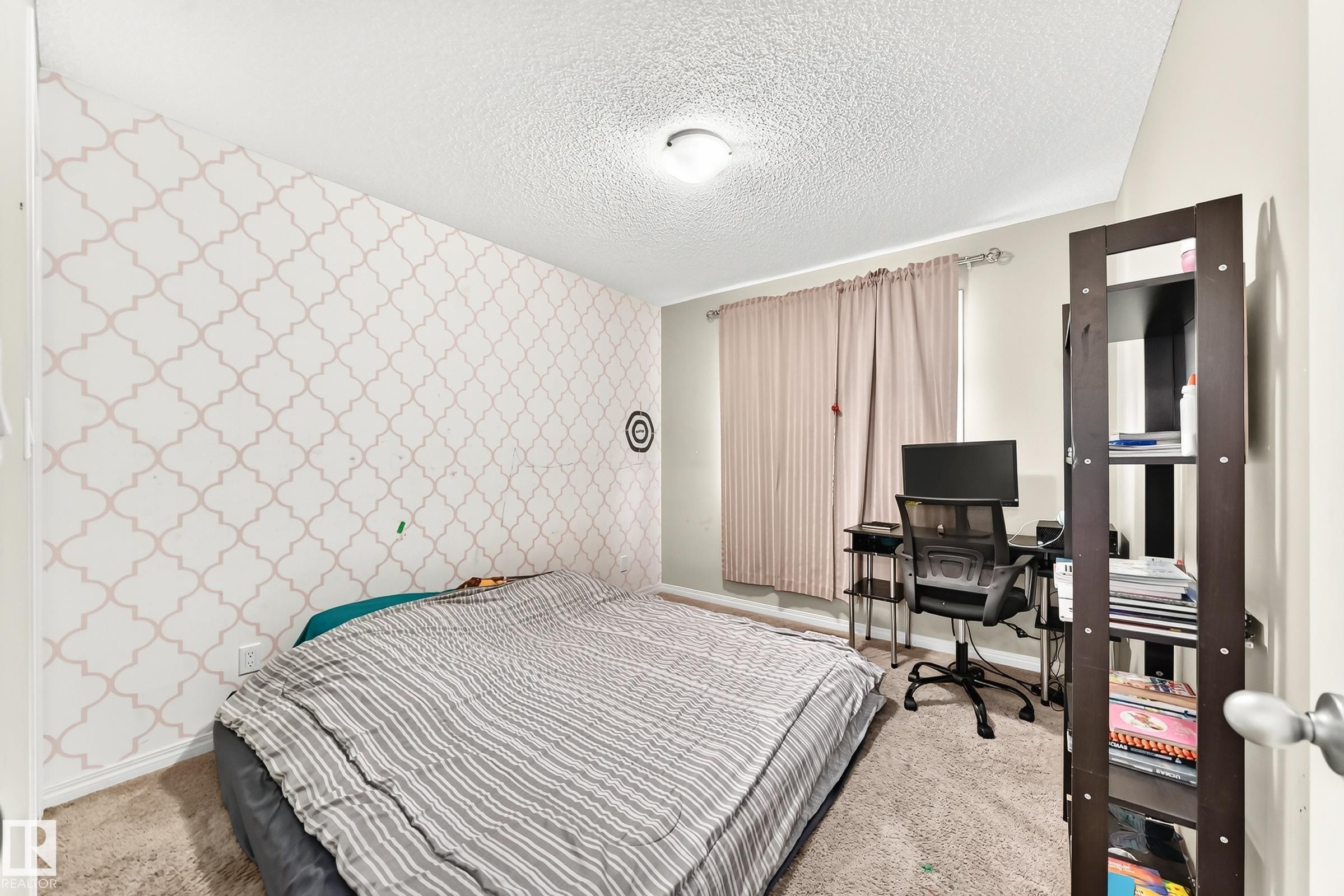 Carpeted bedroom featuring patterned accent wall, neutral wall paint, and a window with curtains - 875 Chappelle Link Link Sw, Edmonton, AB