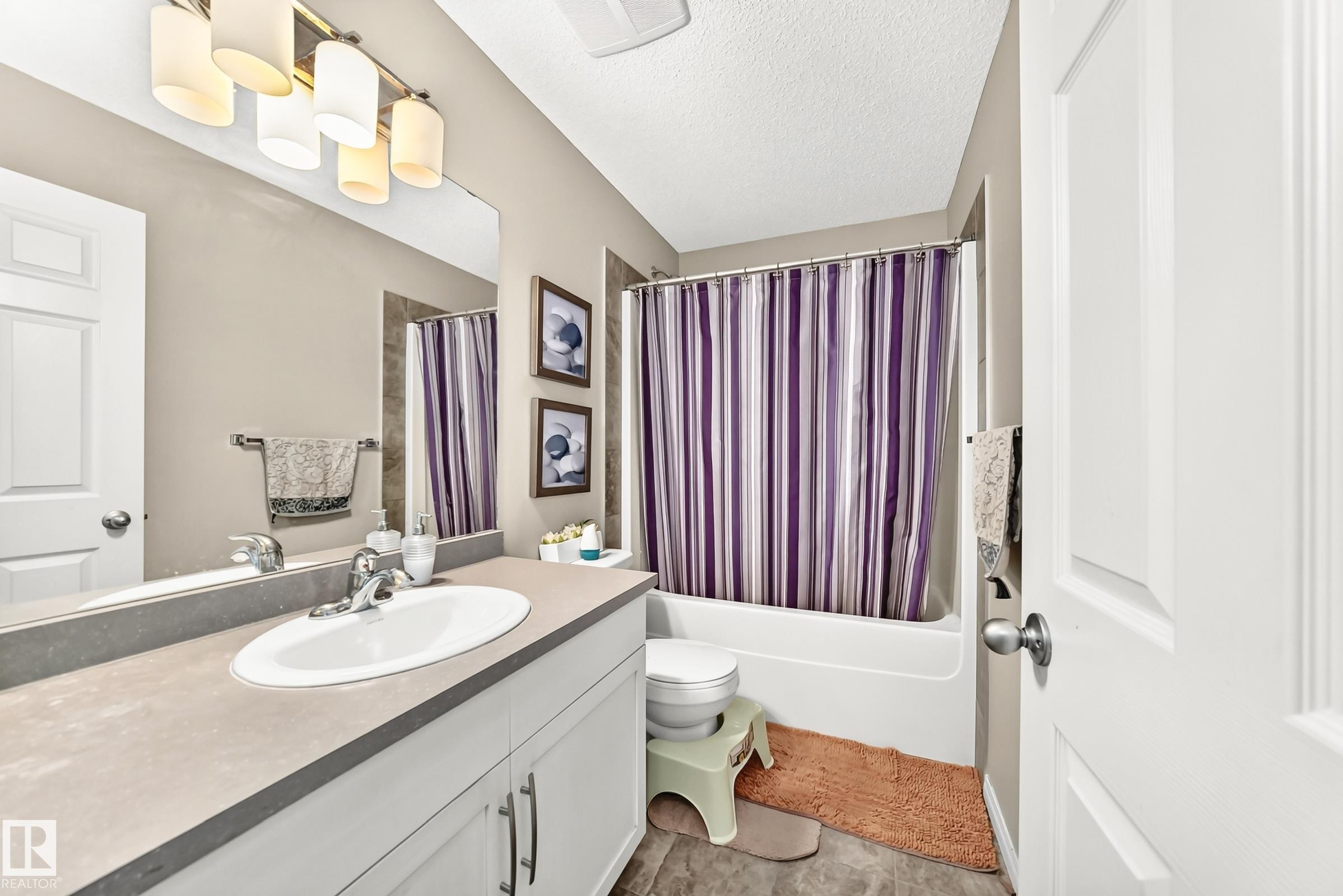 Full bathroom featuring a single vanity with an integrated sink, a large wall-mounted mirror, white shaker-style cabinetry, and a combination shower-tub unit - 875 Chappelle Link Link Sw, Edmonton, AB