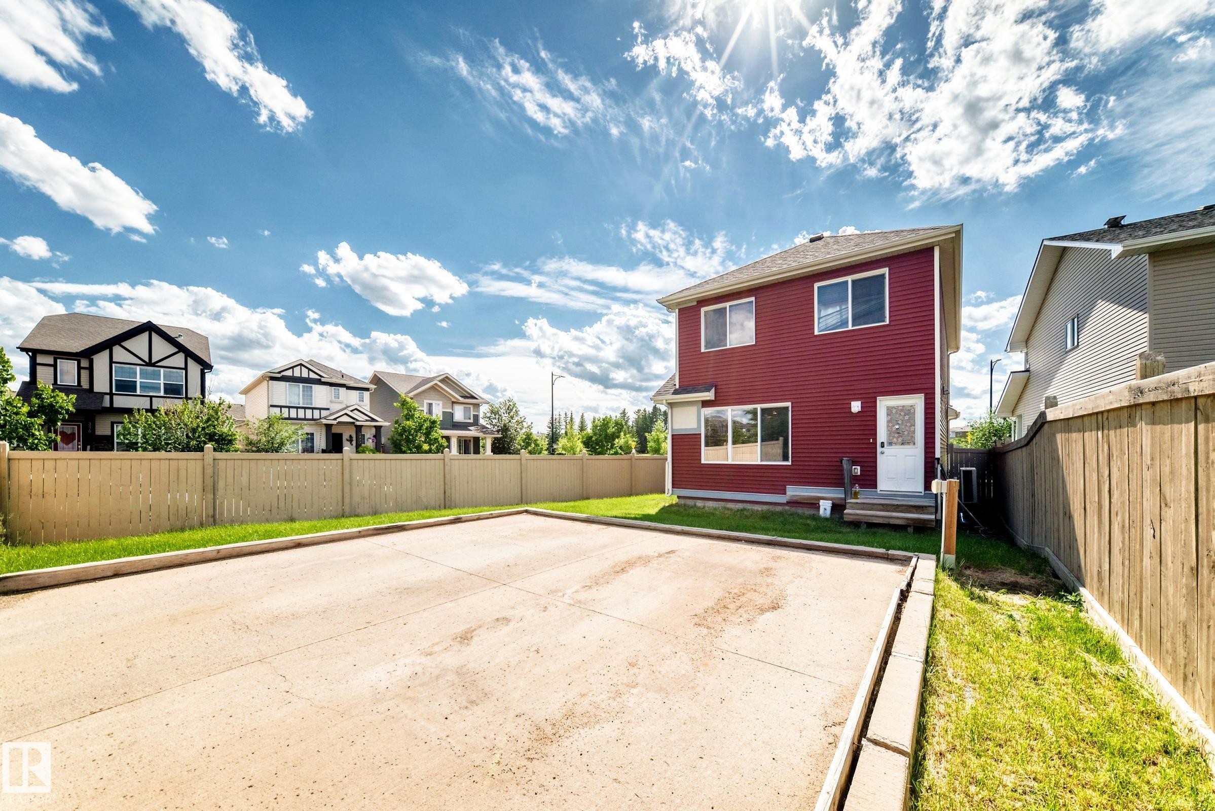 Red siding exterior with a white rear entry door, featuring a concrete pad and wooden fencing - 875 Chappelle Link Link Sw, Edmonton, AB