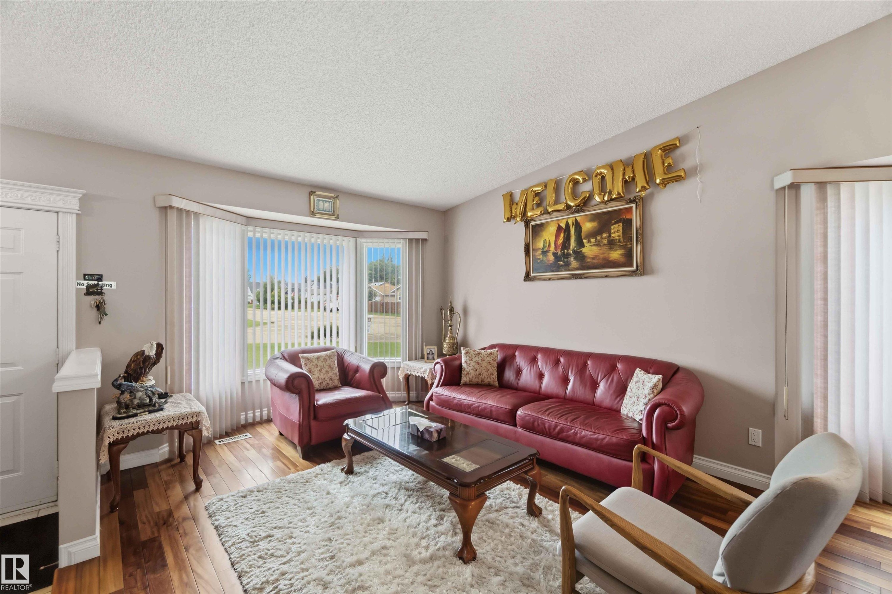 Living area featuring wood-finish flooring, a large bay window with vertical blinds, and neutral wall paint - 4428 11A Avenue Nw, Edmonton, AB - Indoor Photo Showing Living Room