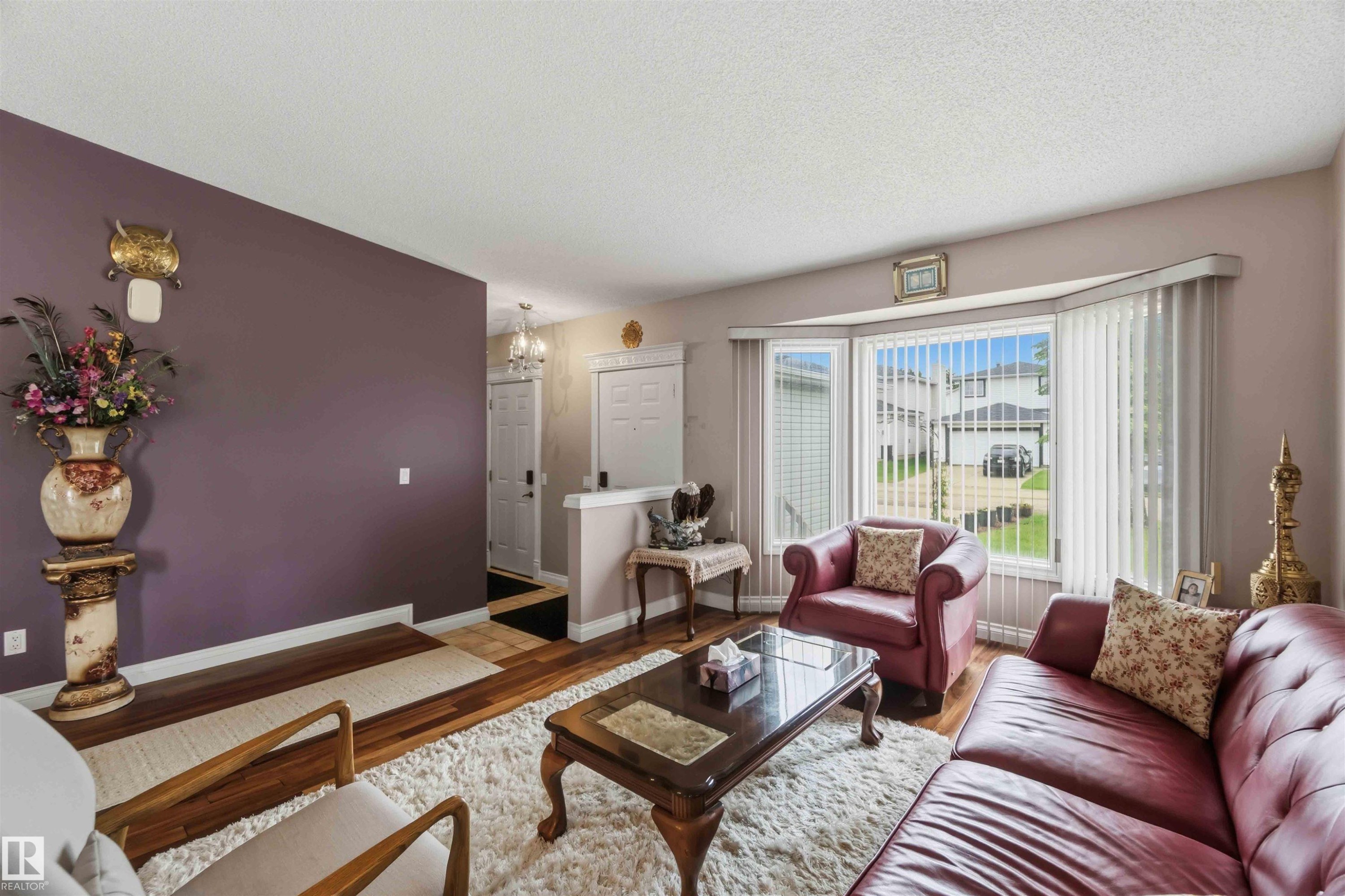 Spacious living area featuring wood-finish flooring, a prominent bay window with vertical blinds, and a neutral color palette - 4428 11A Avenue Nw, Edmonton, AB - Indoor Photo Showing Living Room