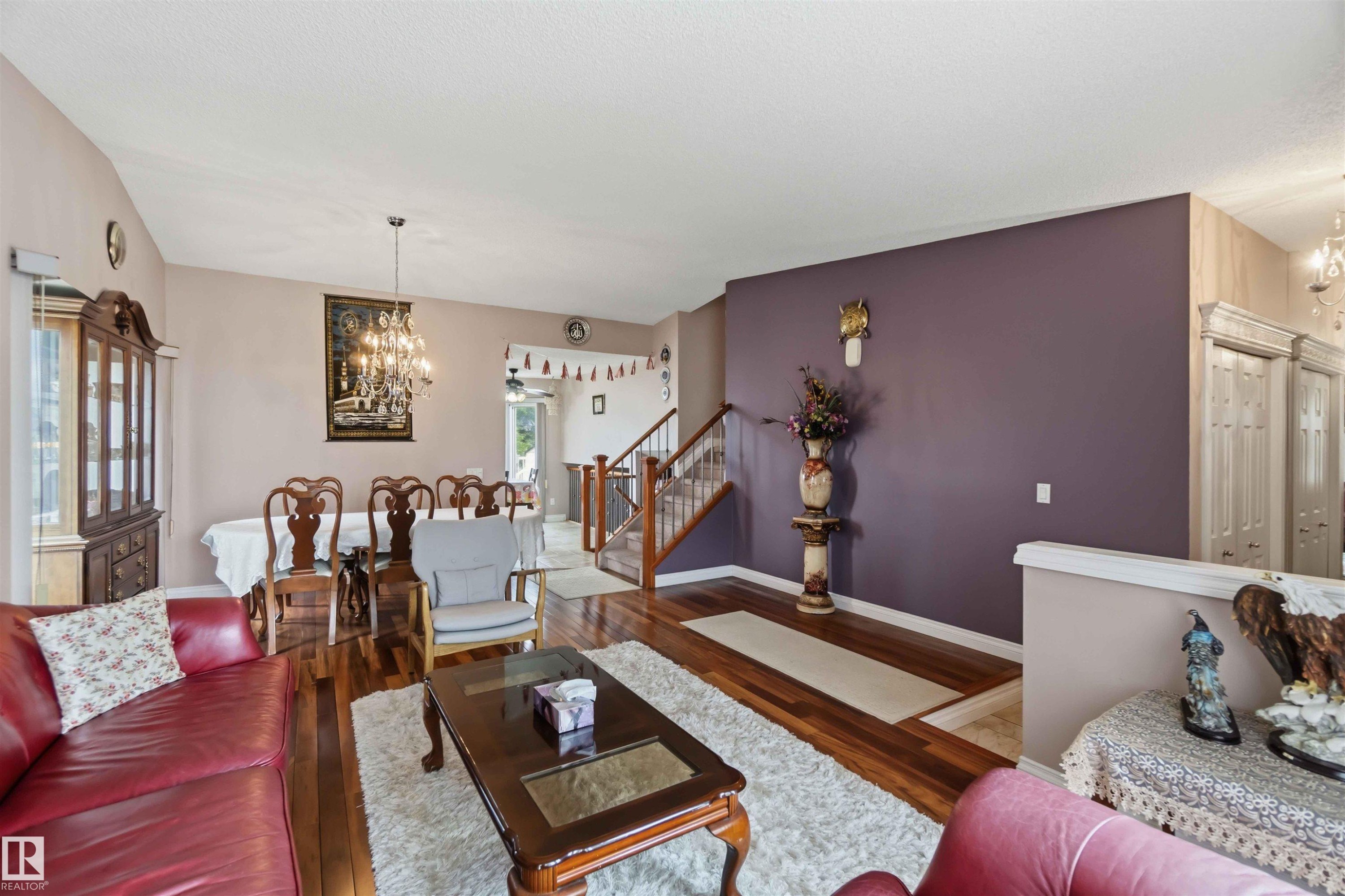 Spacious living area featuring wood-finish flooring, a formal dining space with chandelier, and a prominent staircase with wooden railings - 4428 11A Avenue Nw, Edmonton, AB - Indoor Photo Showing Living Room