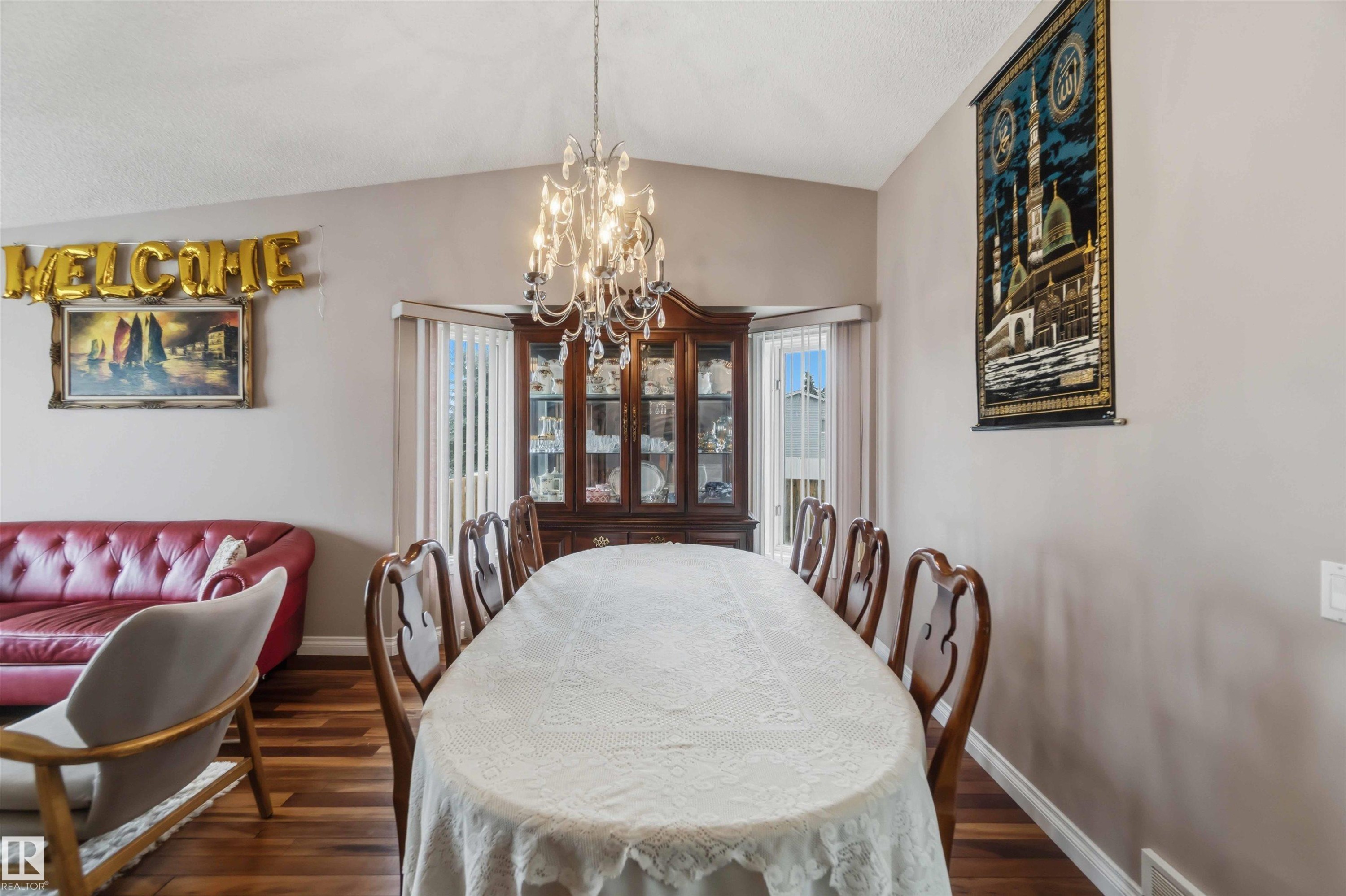 Formal dining area featuring wood-finish flooring, a tiered crystal chandelier, and a bay window with vertical blinds - 4428 11A Avenue Nw, Edmonton, AB - Indoor Photo Showing Dining Room