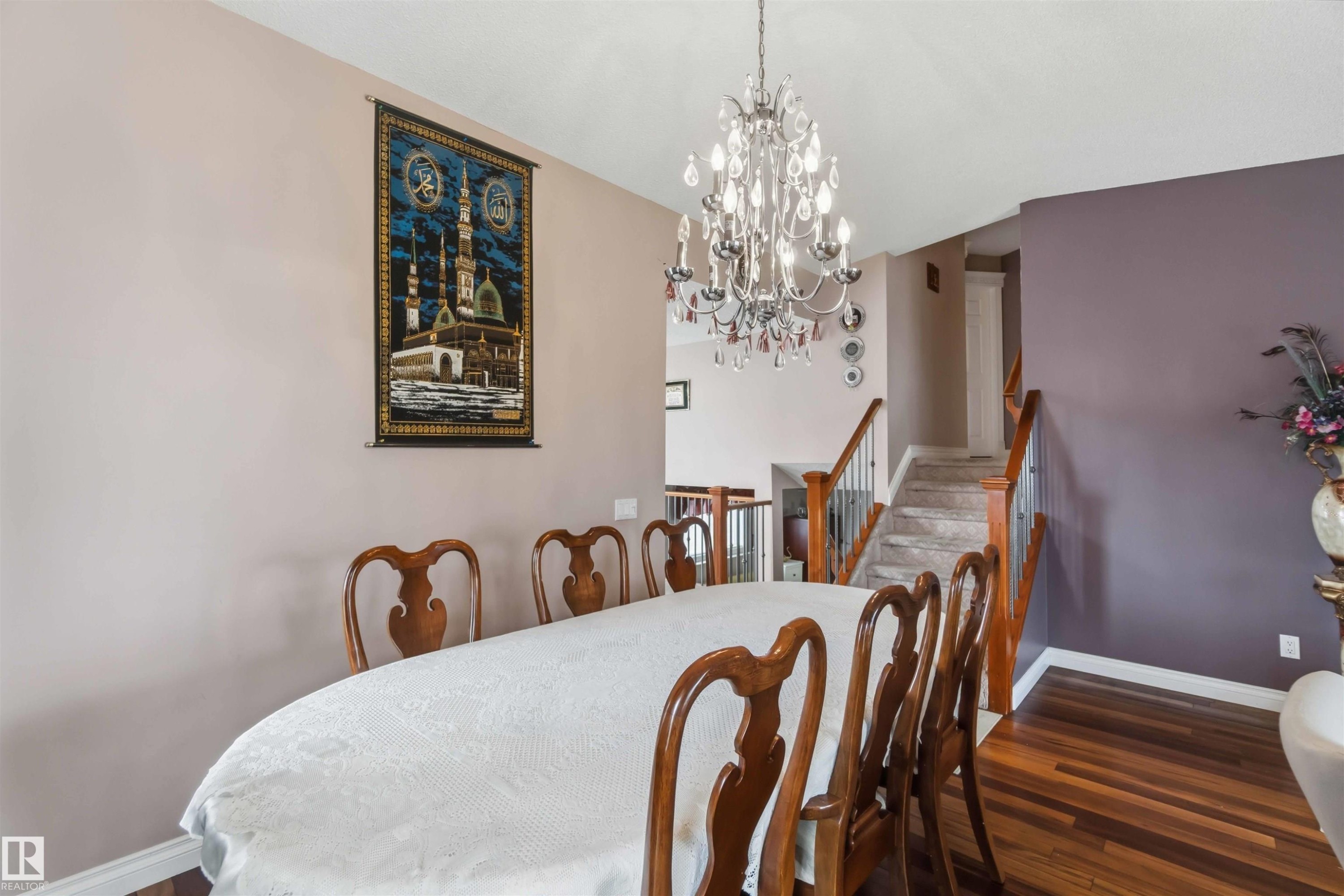 Dining area with wood-finish flooring, a tiered crystal chandelier, and a staircase featuring wood railings with metal balusters - 4428 11A Avenue Nw, Edmonton, AB - Indoor Photo Showing Dining Room