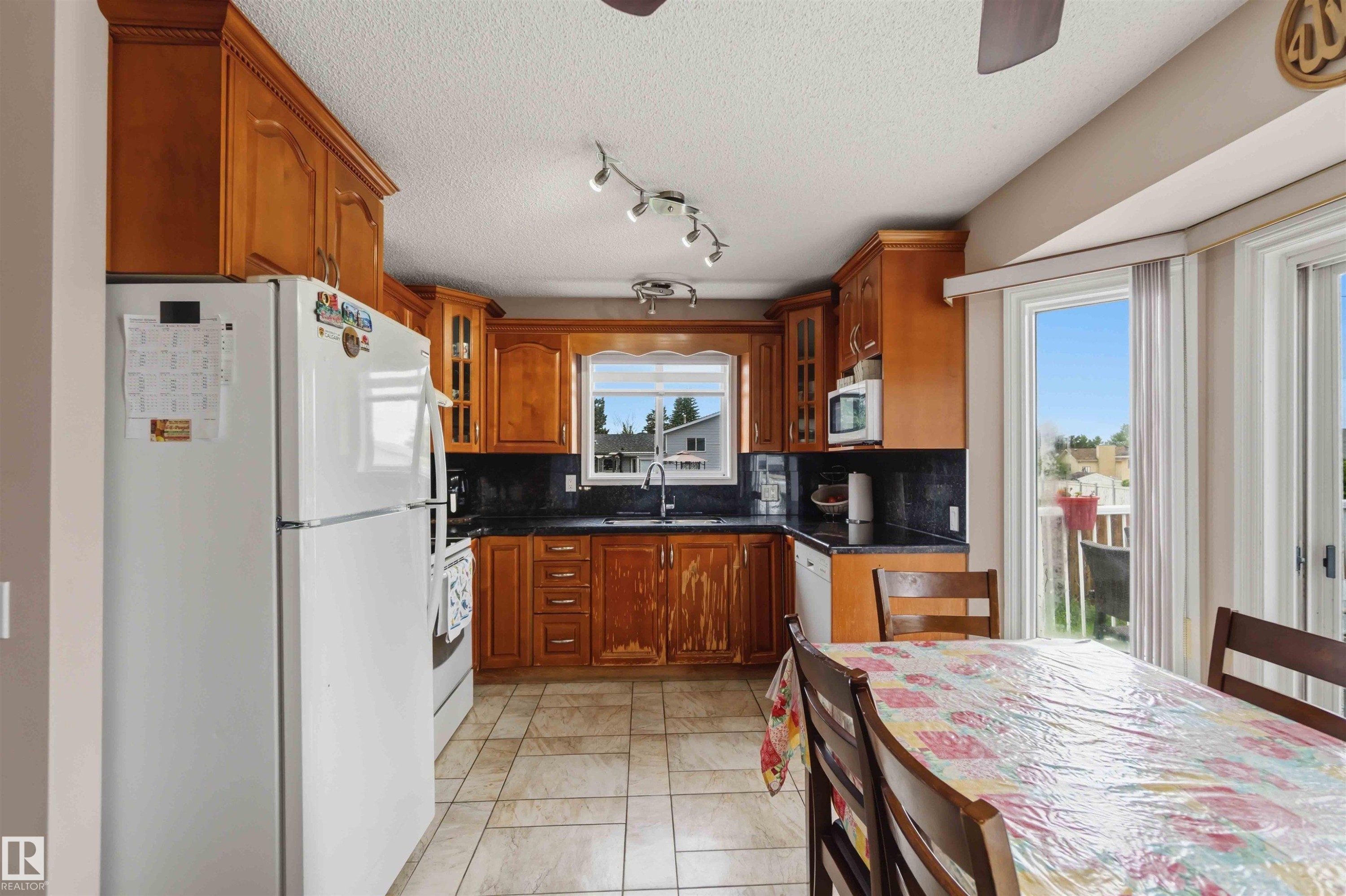 Kitchen featuring wood cabinetry, dark countertops, tiled flooring, track lighting, and a window above the sink - 4428 11A Avenue Nw, Edmonton, AB - Indoor Photo Showing Other Room