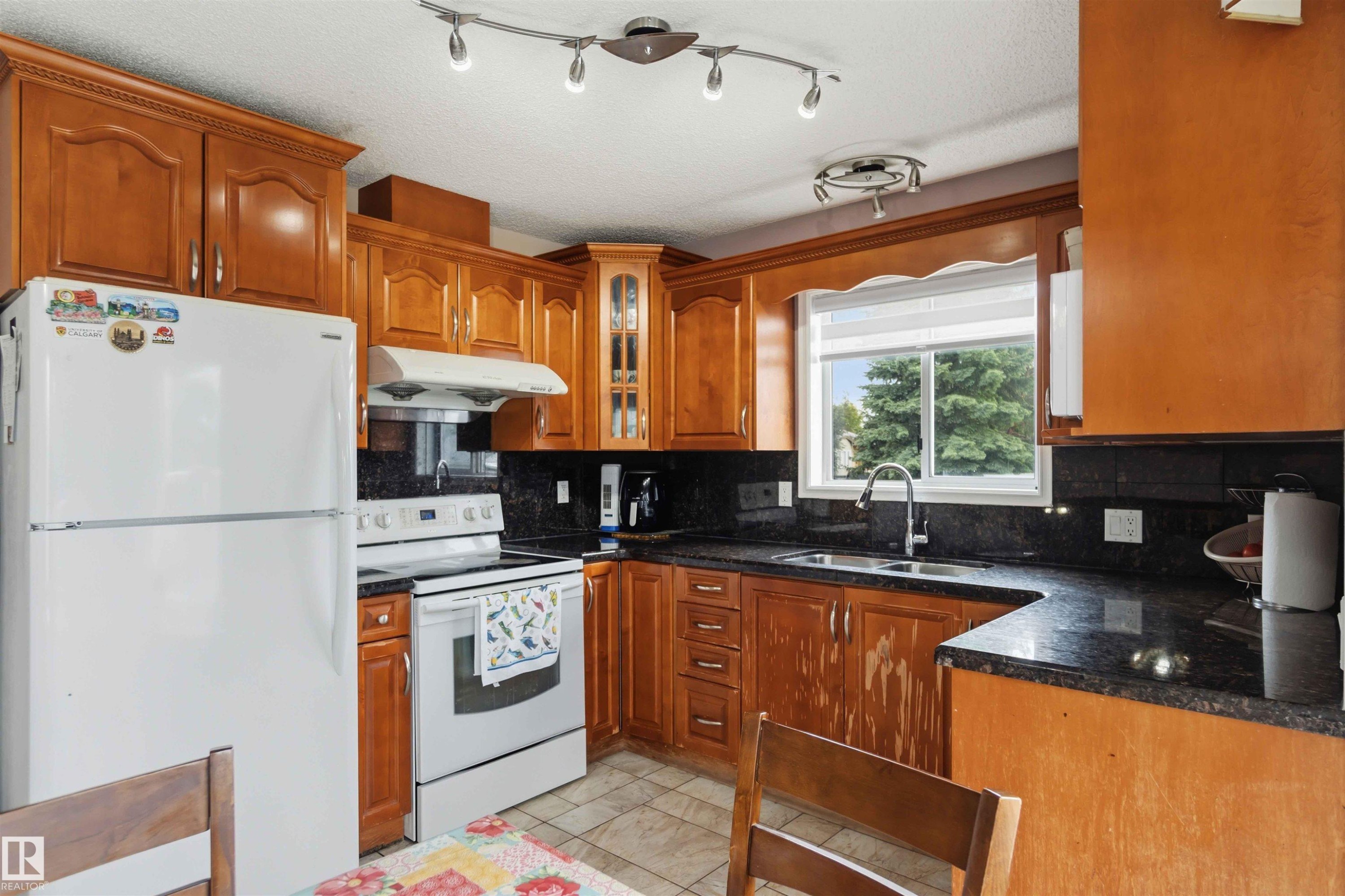Kitchen with wood cabinetry, dark countertops, tile flooring, a double basin sink, and a window above the sink - 4428 11A Avenue Nw, Edmonton, AB - Indoor Photo Showing Kitchen With Double Sink