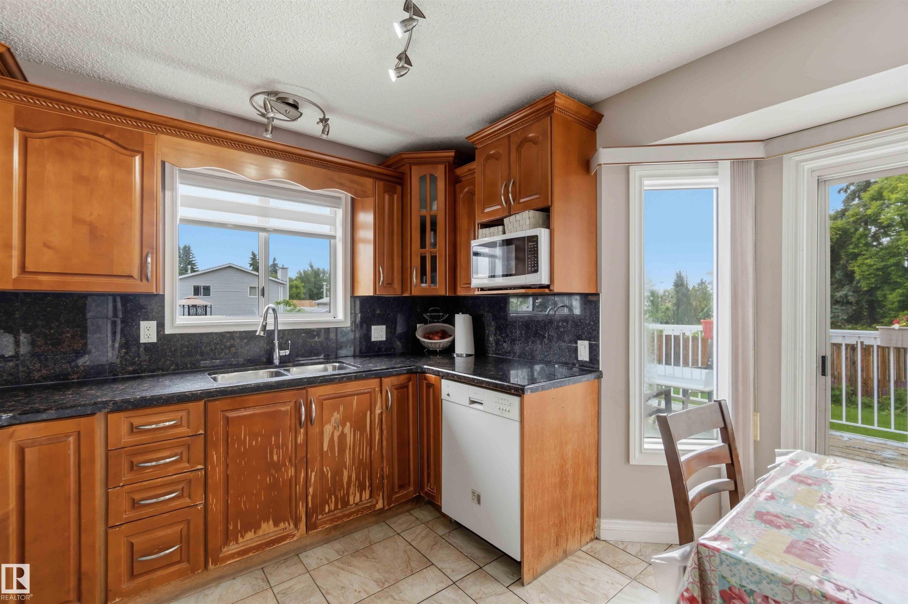 Kitchen featuring wood cabinetry, dark countertops, and tile flooring - 4428 11A Avenue Nw, Edmonton, AB - Indoor Photo Showing Kitchen With Double Sink