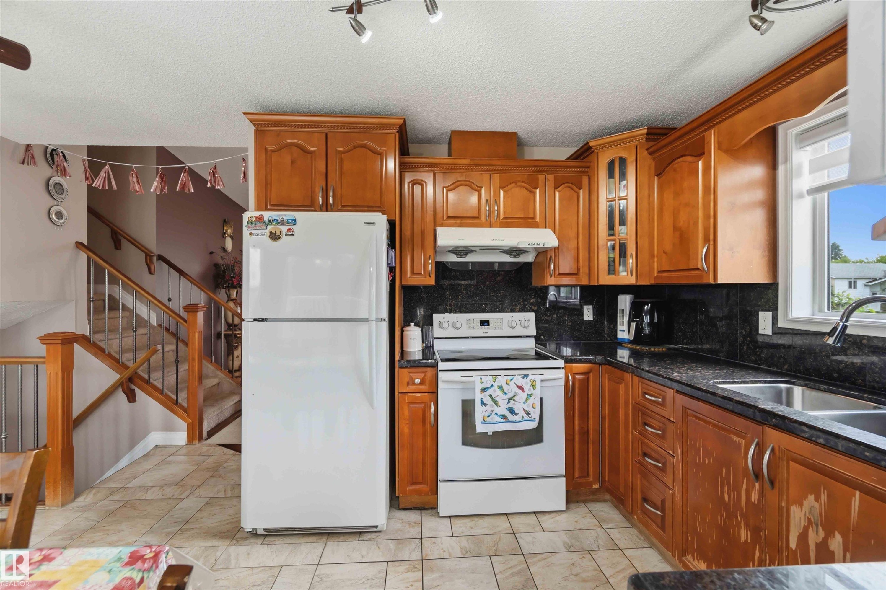 Kitchen featuring wood cabinetry, dark countertops, a double basin stainless steel sink, and a white electric range - 4428 11A Avenue Nw, Edmonton, AB - Indoor Photo Showing Kitchen
