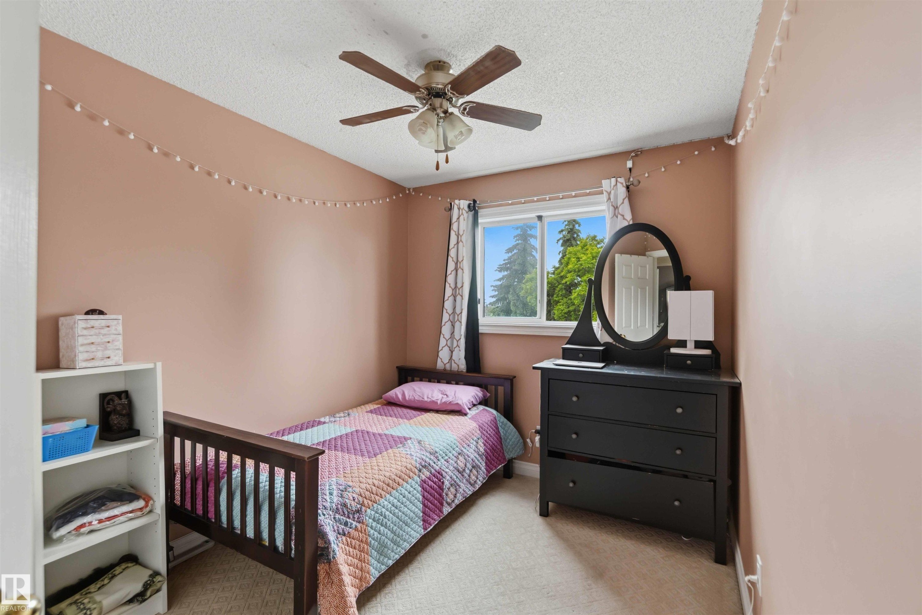 Bedroom featuring a window with exterior tree views, a ceiling fan, light beige carpeting, and painted walls - 4428 11A Avenue Nw, Edmonton, AB - Indoor Photo Showing Bedroom