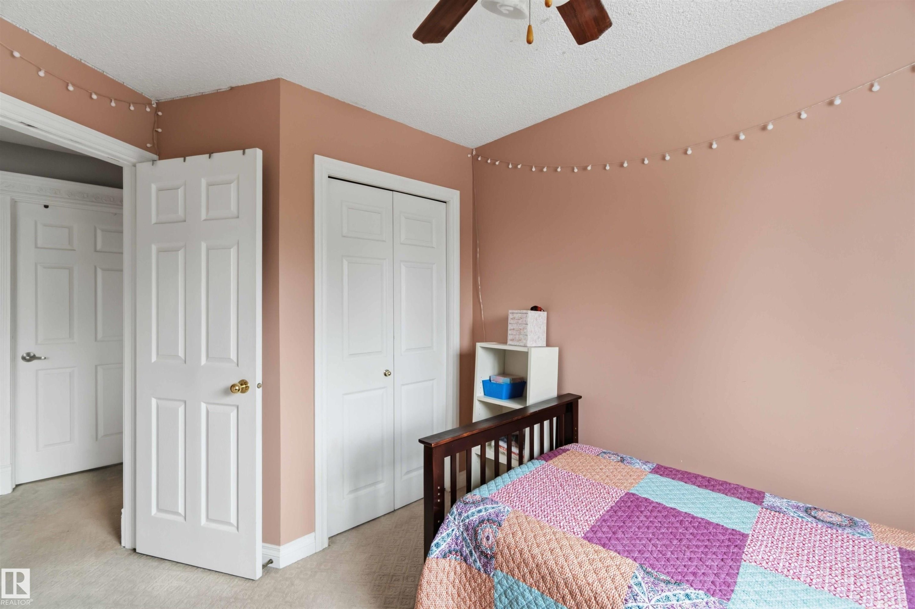 Room featuring two white paneled doors, a bi-fold closet, textured ceiling, and light-colored carpeting - 4428 11A Avenue Nw, Edmonton, AB - Indoor Photo Showing Bedroom
