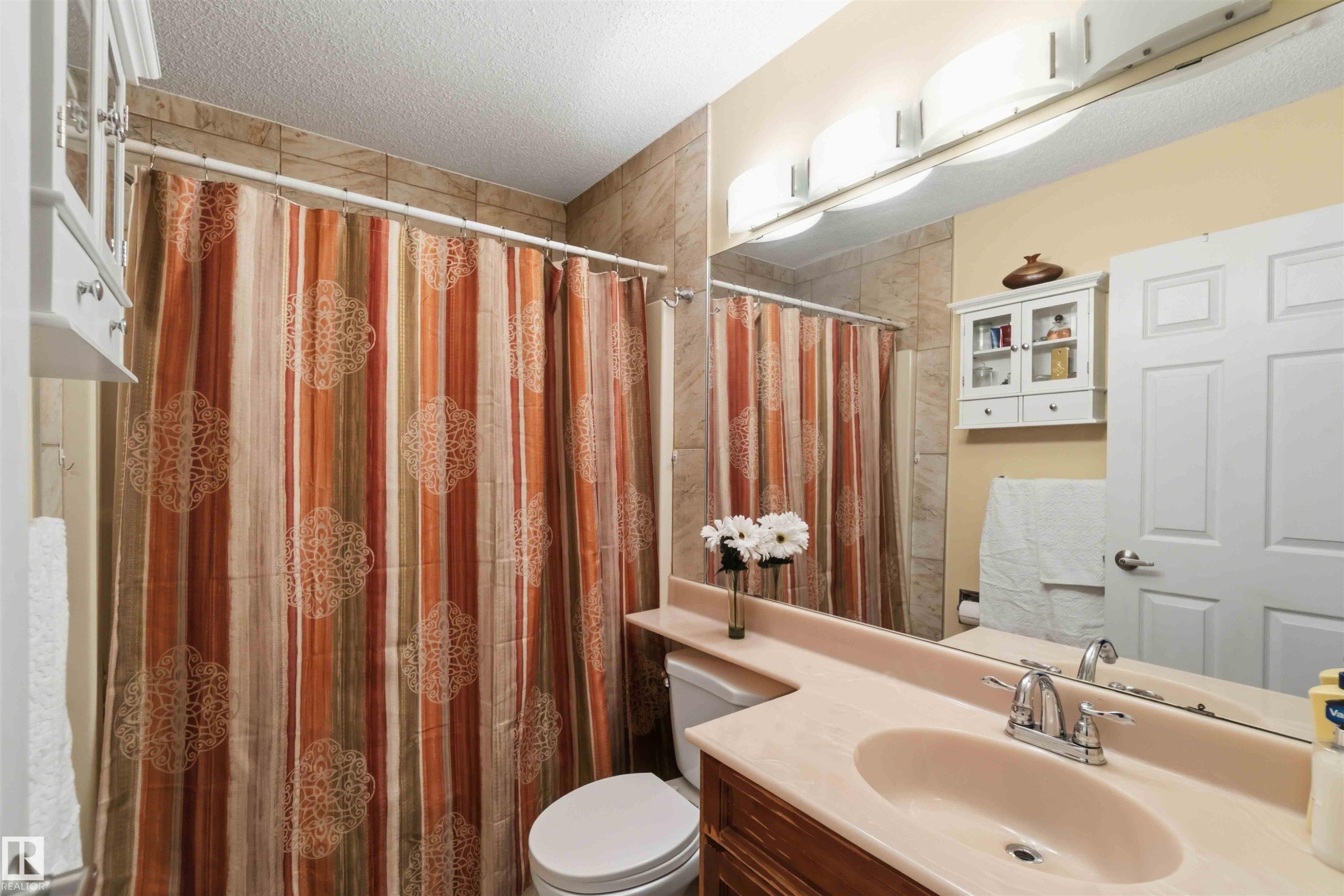 Bathroom featuring a vanity with an integrated sink, a large wall-mounted mirror, and tile-surround shower - 4428 11A Avenue Nw, Edmonton, AB - Indoor Photo Showing Bathroom