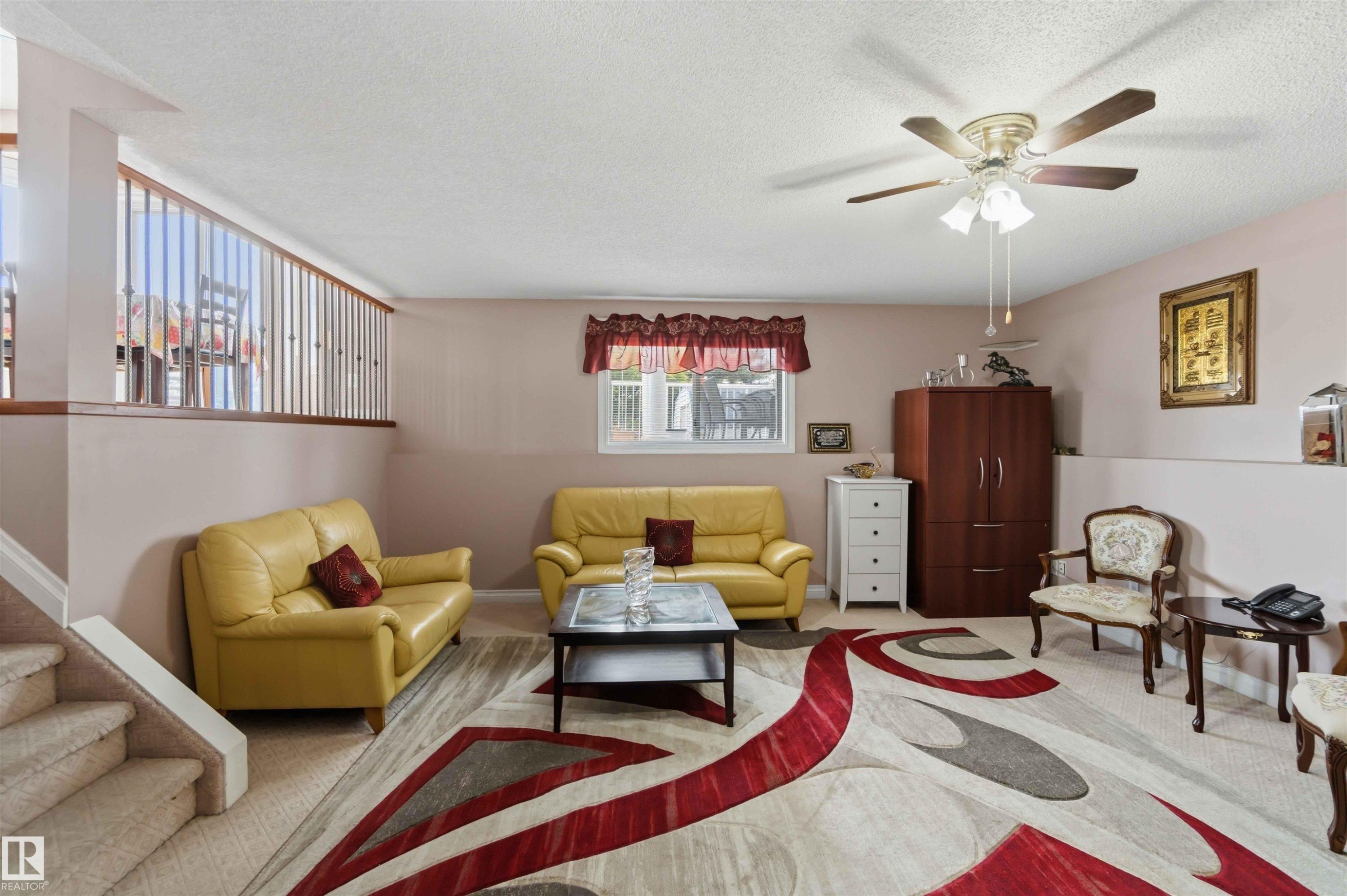 Carpeted living area featuring a ceiling fan with integrated lighting, a window with valance, and a half-wall with wood railing - 4428 11A Avenue Nw, Edmonton, AB - Indoor Photo Showing Other Room