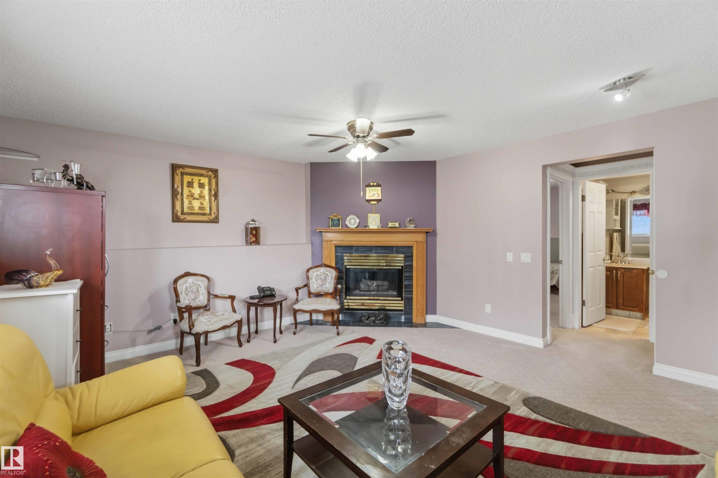 Living area with a ceiling fan, light-colored carpet, and a fireplace featuring a black tile surround and wood mantel - 4428 11A Avenue Nw, Edmonton, AB - Indoor Photo Showing Living Room With Fireplace
