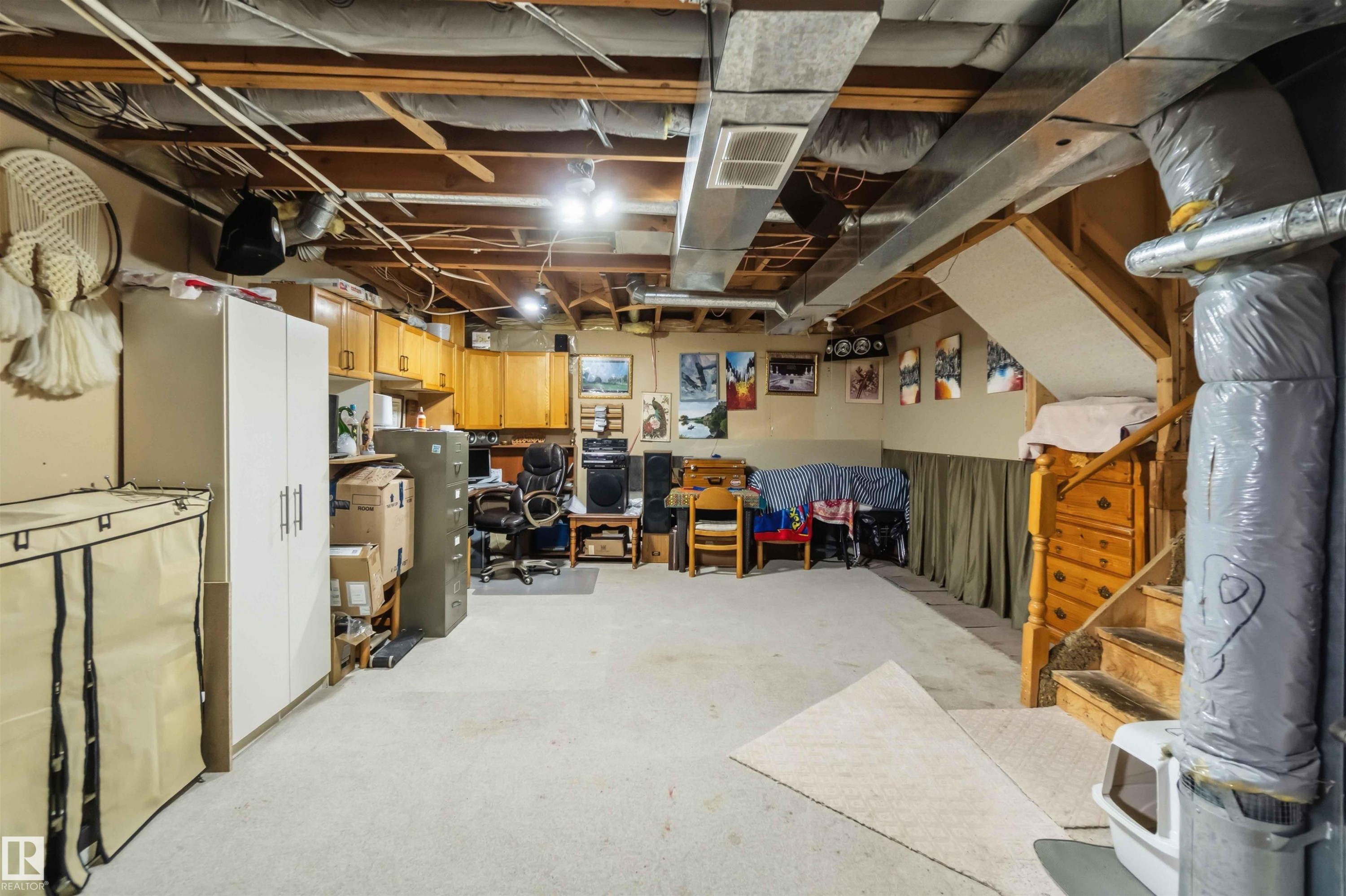 Carpeted basement with exposed ceiling beams and ductwork, featuring wood-finish cabinetry, built-in shelving, and a wooden staircase - 4428 11A Avenue Nw, Edmonton, AB - Indoor Photo Showing Basement
